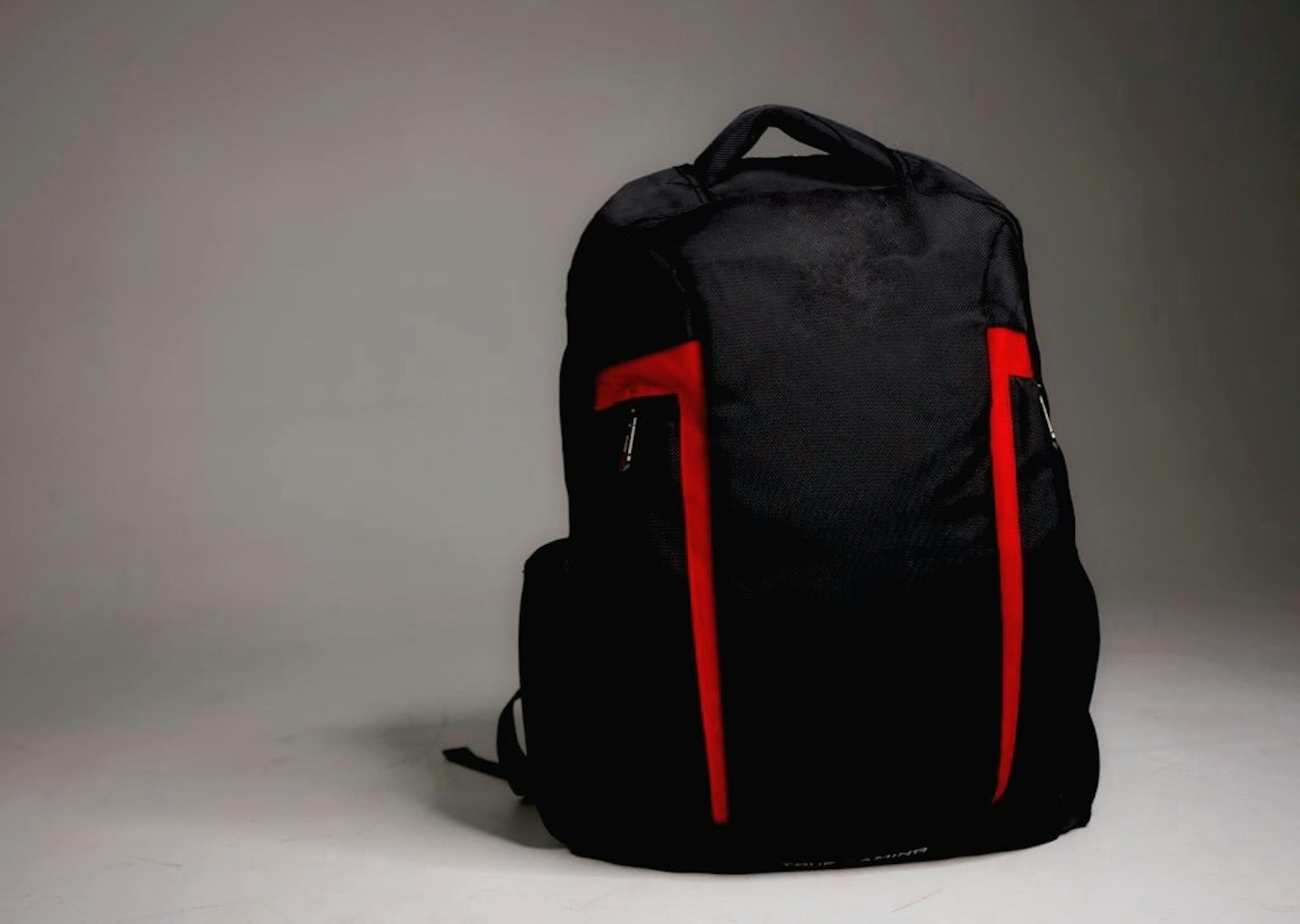 Ein schwarzer Rucksack mit roten Akzenten vor einem neutralen Hintergrund