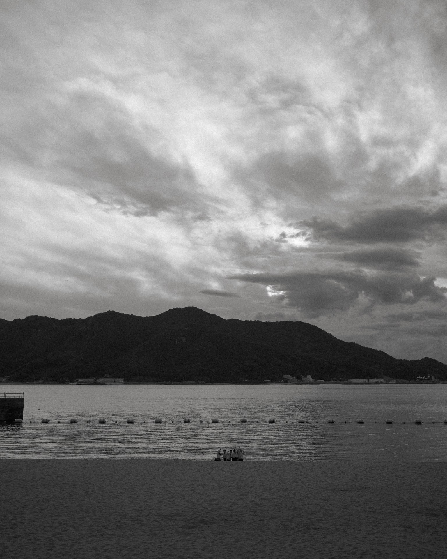 Image en noir et blanc d'une plage avec des montagnes et un ciel nuageux