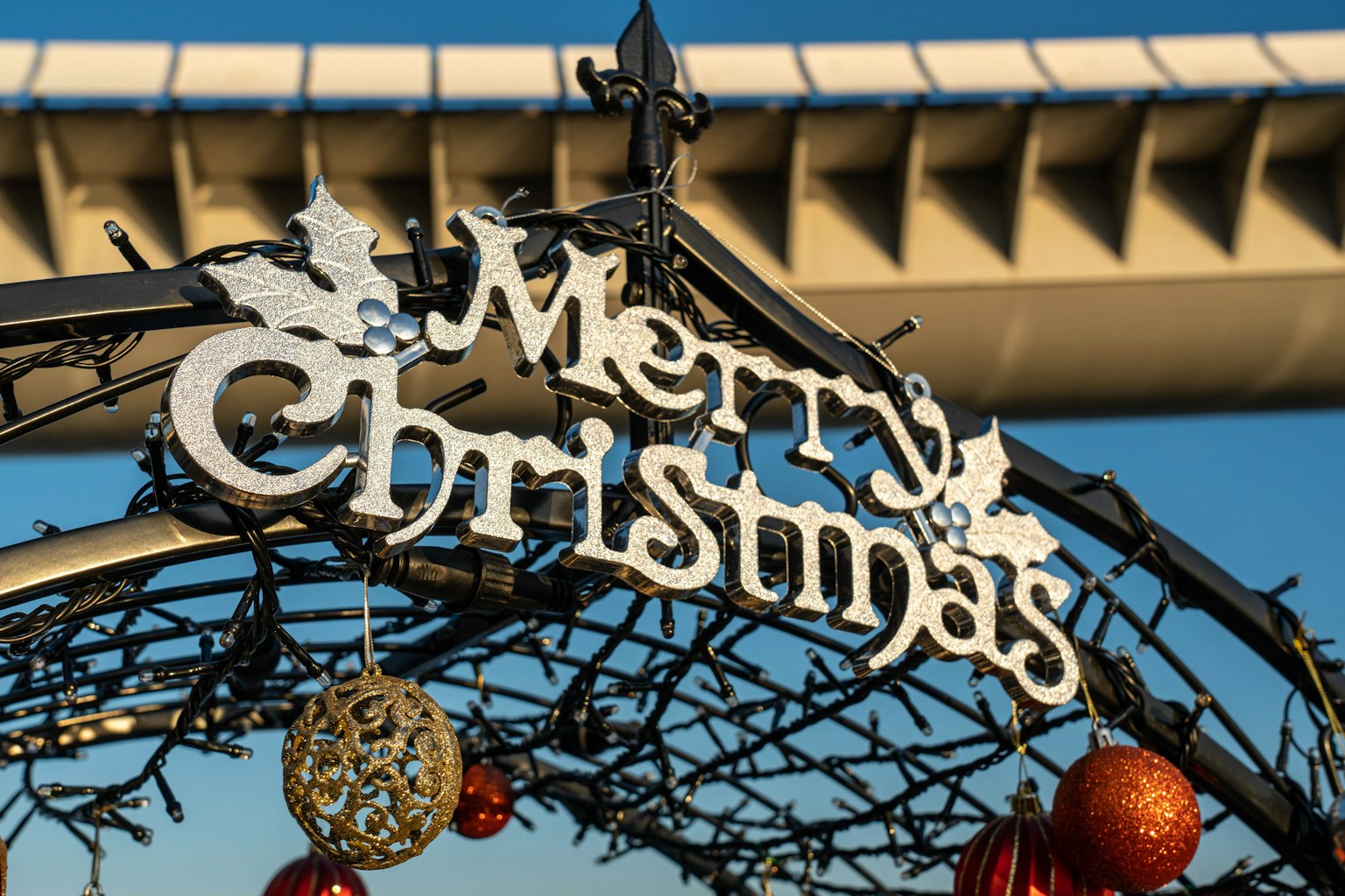 Sebuah lengkungan dekoratif dengan kata Merry Christmas dihiasi dengan ornamen dan elemen perayaan