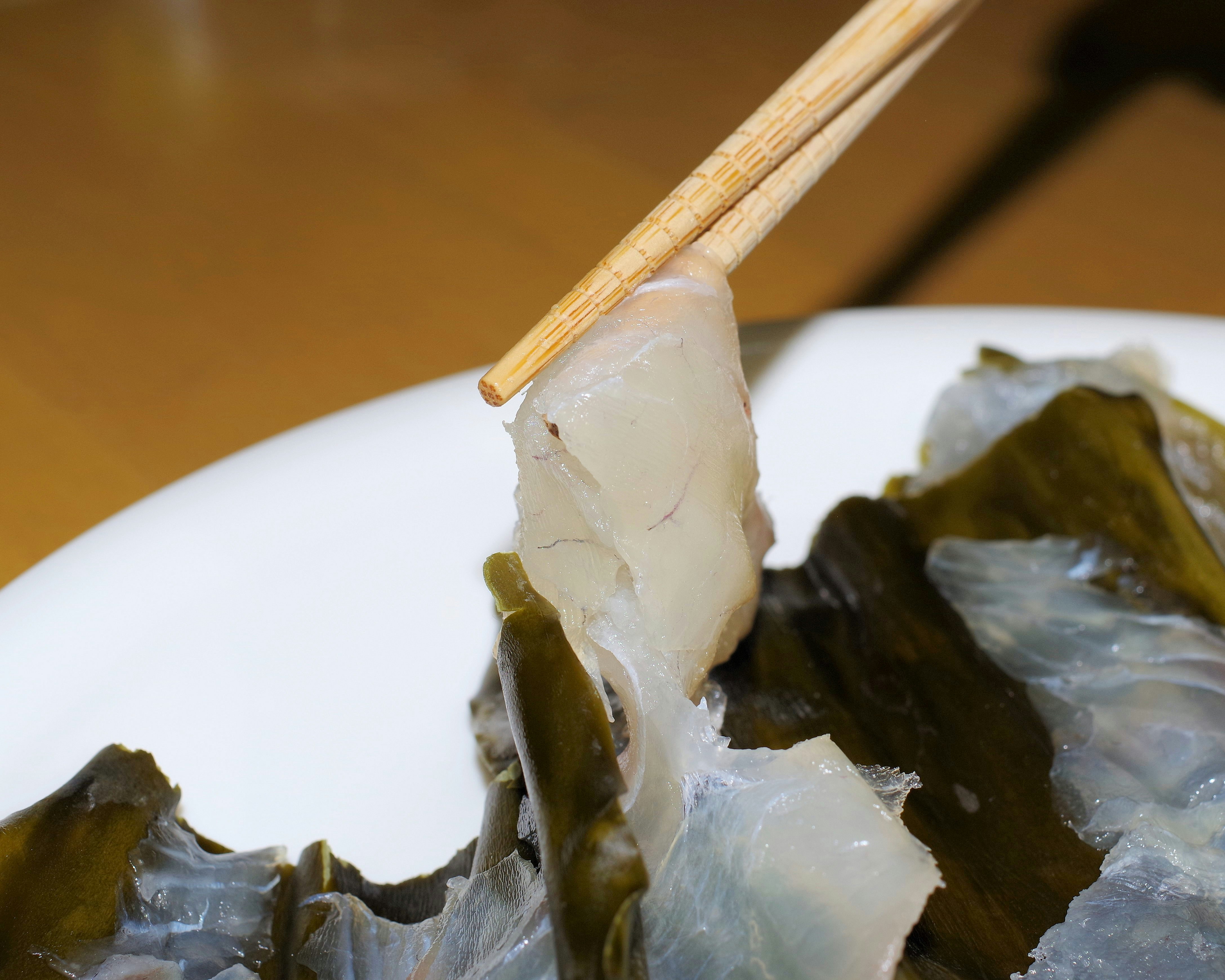 palillos sosteniendo trozos de marisco y algas sobre un plato blanco