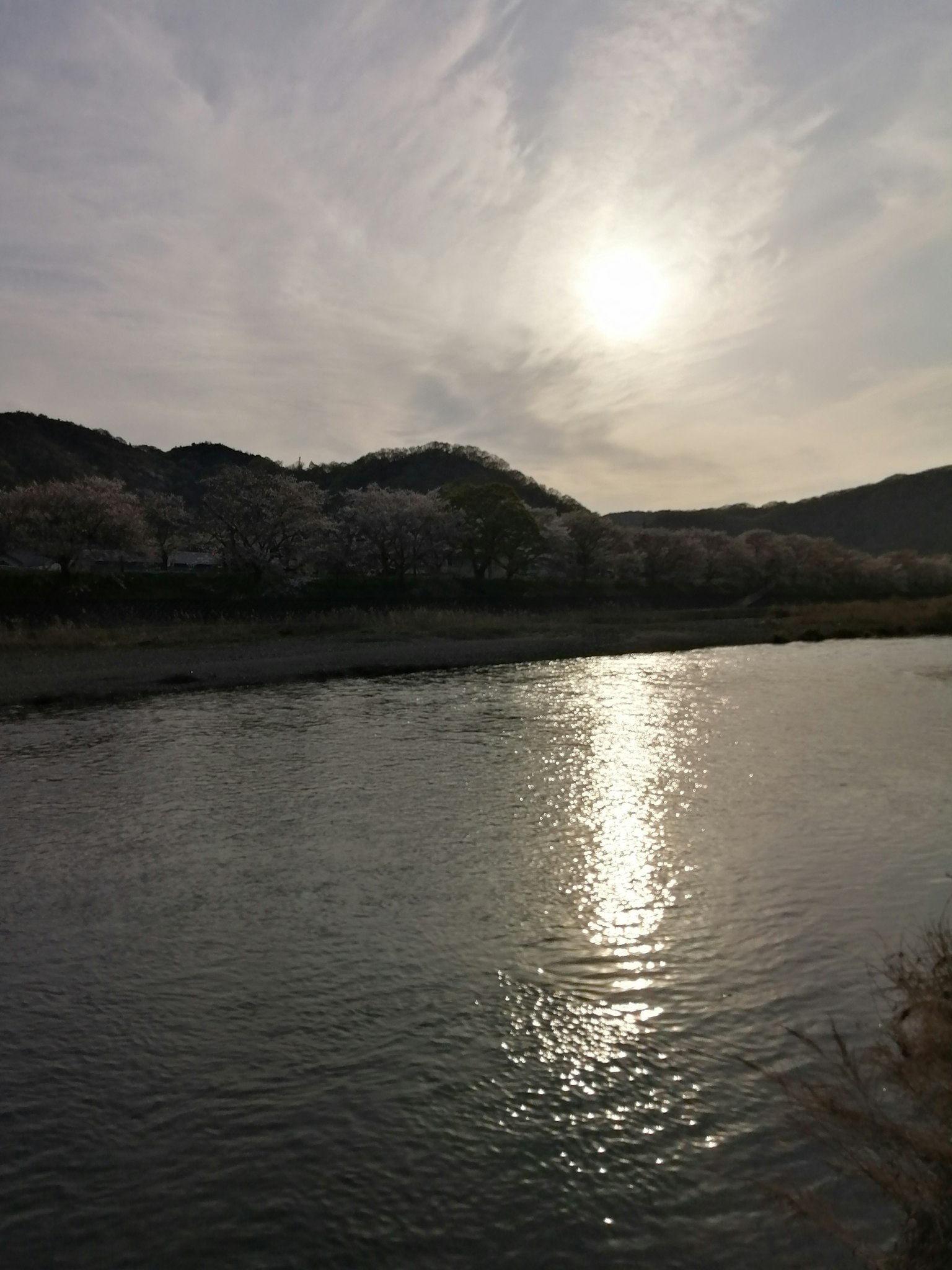 Ruhiger Fluss, der den Sonnenuntergang mit sanften Hügeln im Hintergrund reflektiert