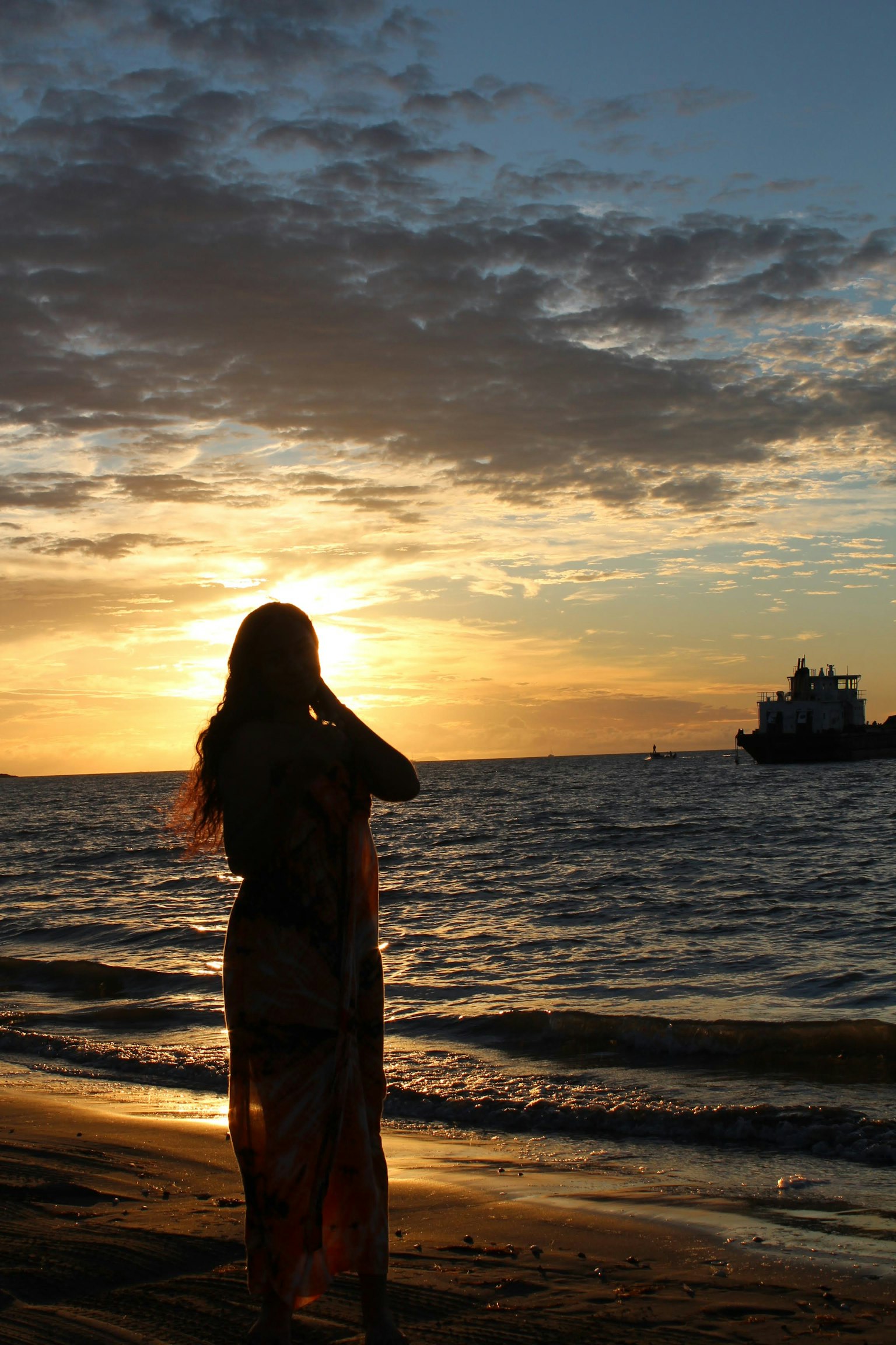 Siluet wanita melawan matahari terbenam di pantai Ombak dan awan berwarna di latar belakang