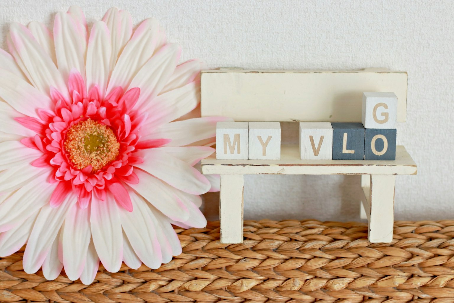 Pequeño banco con bloques de letras que dicen MY VLOG junto a una flor rosa