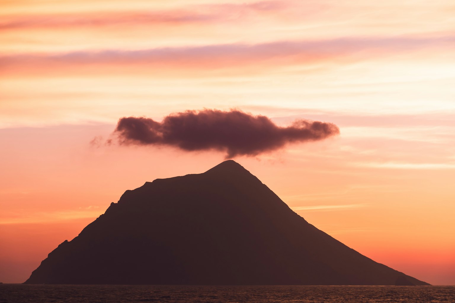 Montagna con una nuvola in cima sotto un cielo al tramonto
