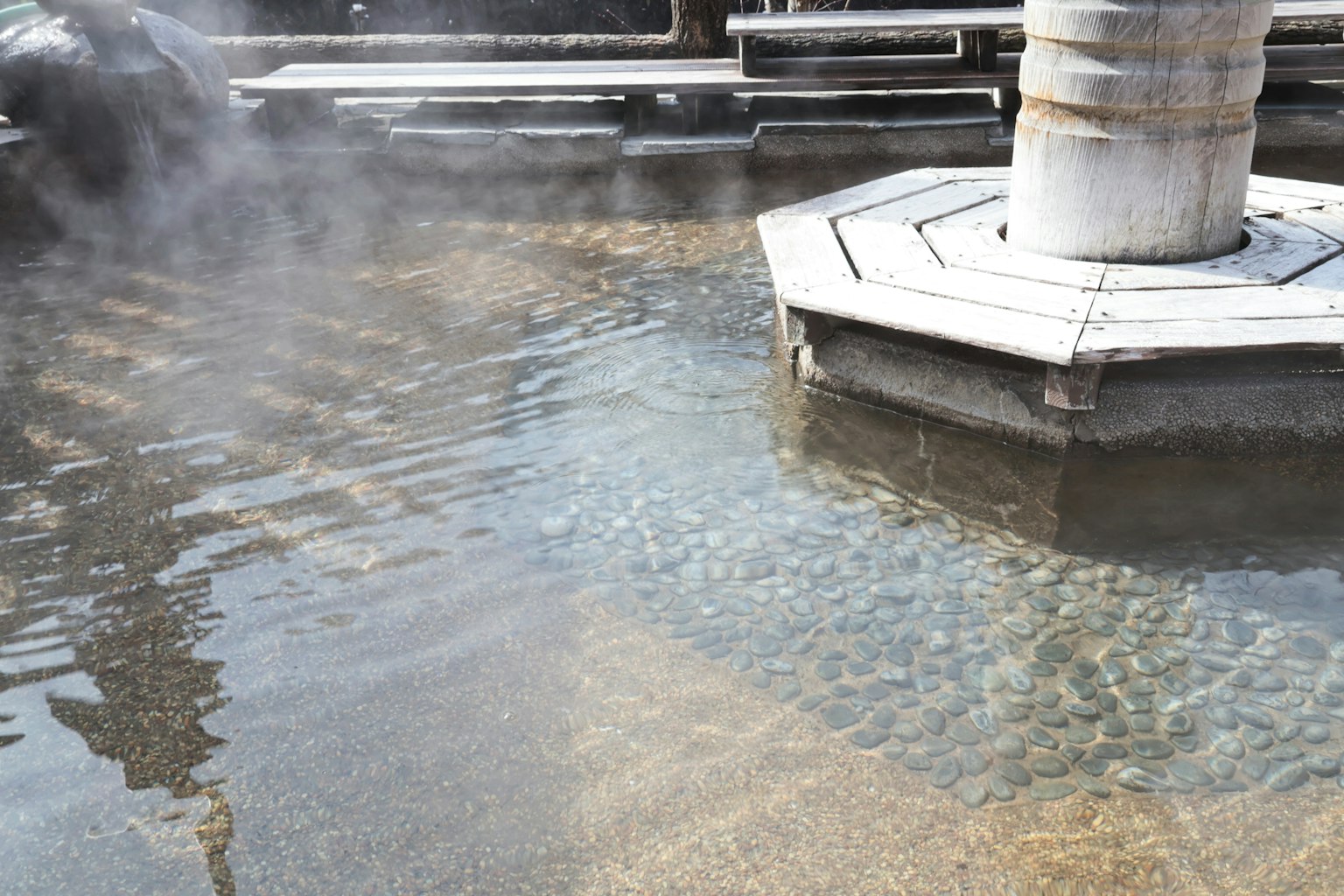 Immagine di una sorgente termale con vapore che sale dalla superficie dell'acqua pietre visibili in acqua bassa
