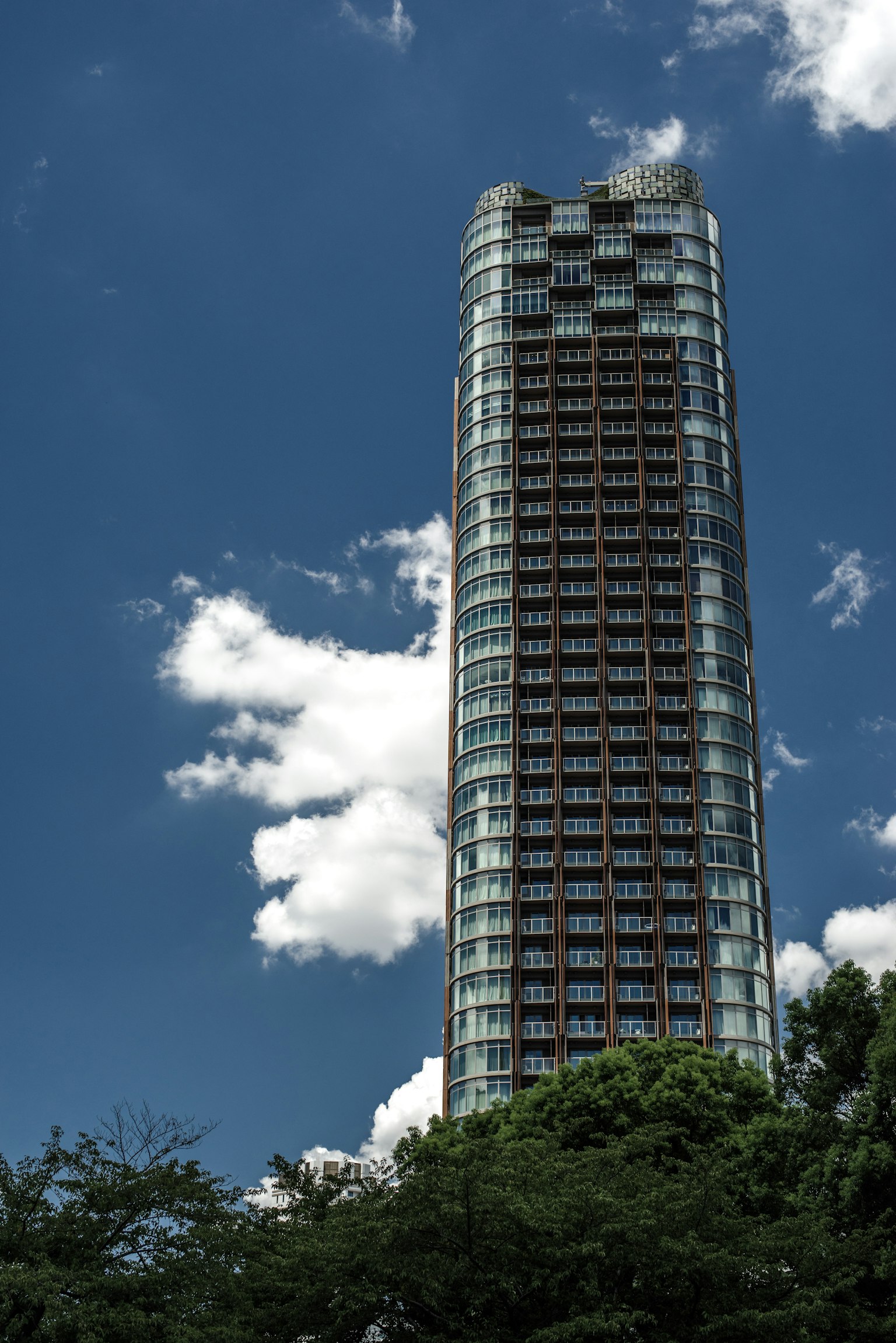 Tall skyscraper with glass facade against a blue sky and white clouds