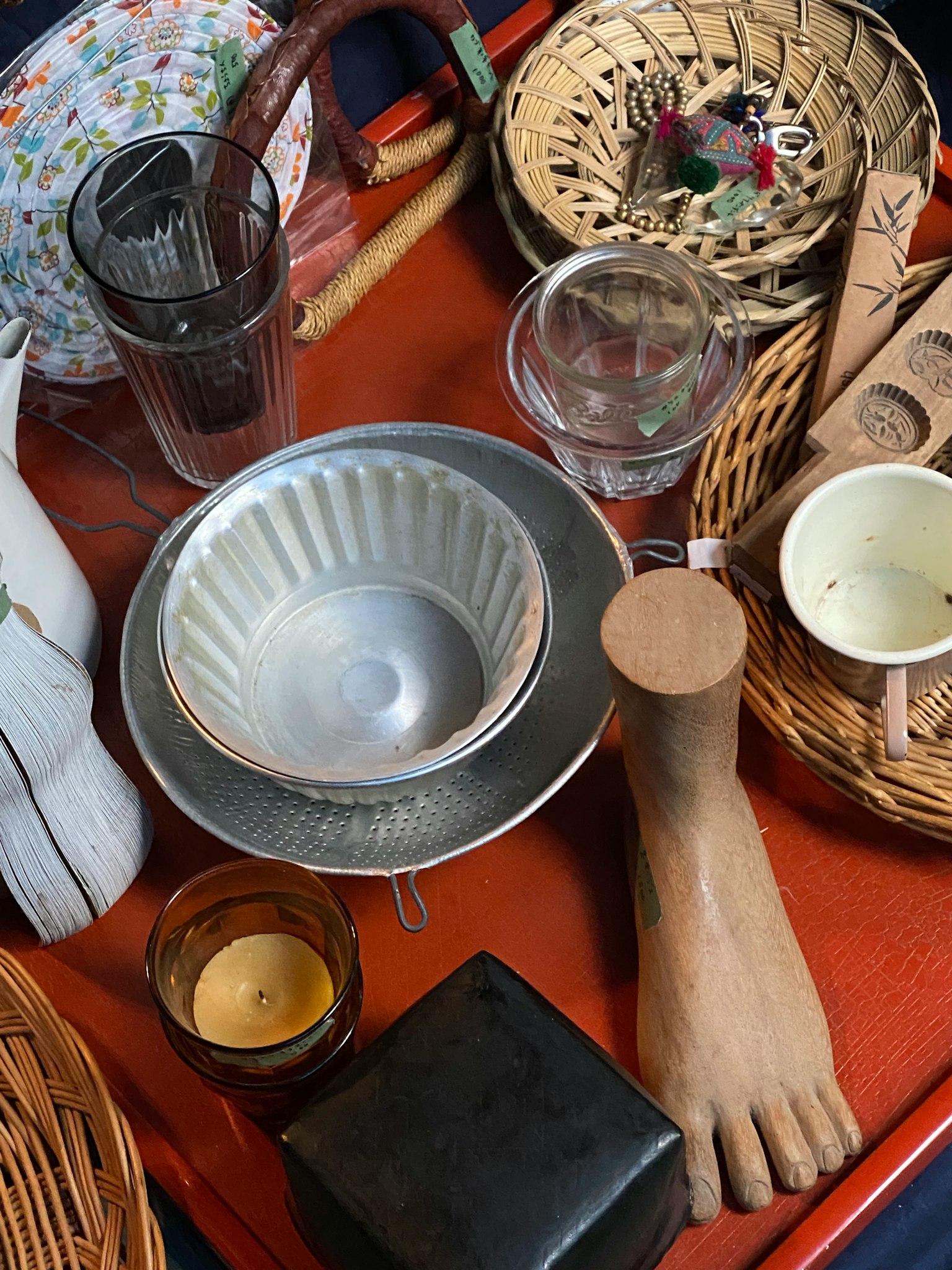 A table displaying various utensils and items including a metal bowl glass cups and a wooden foot sculpture