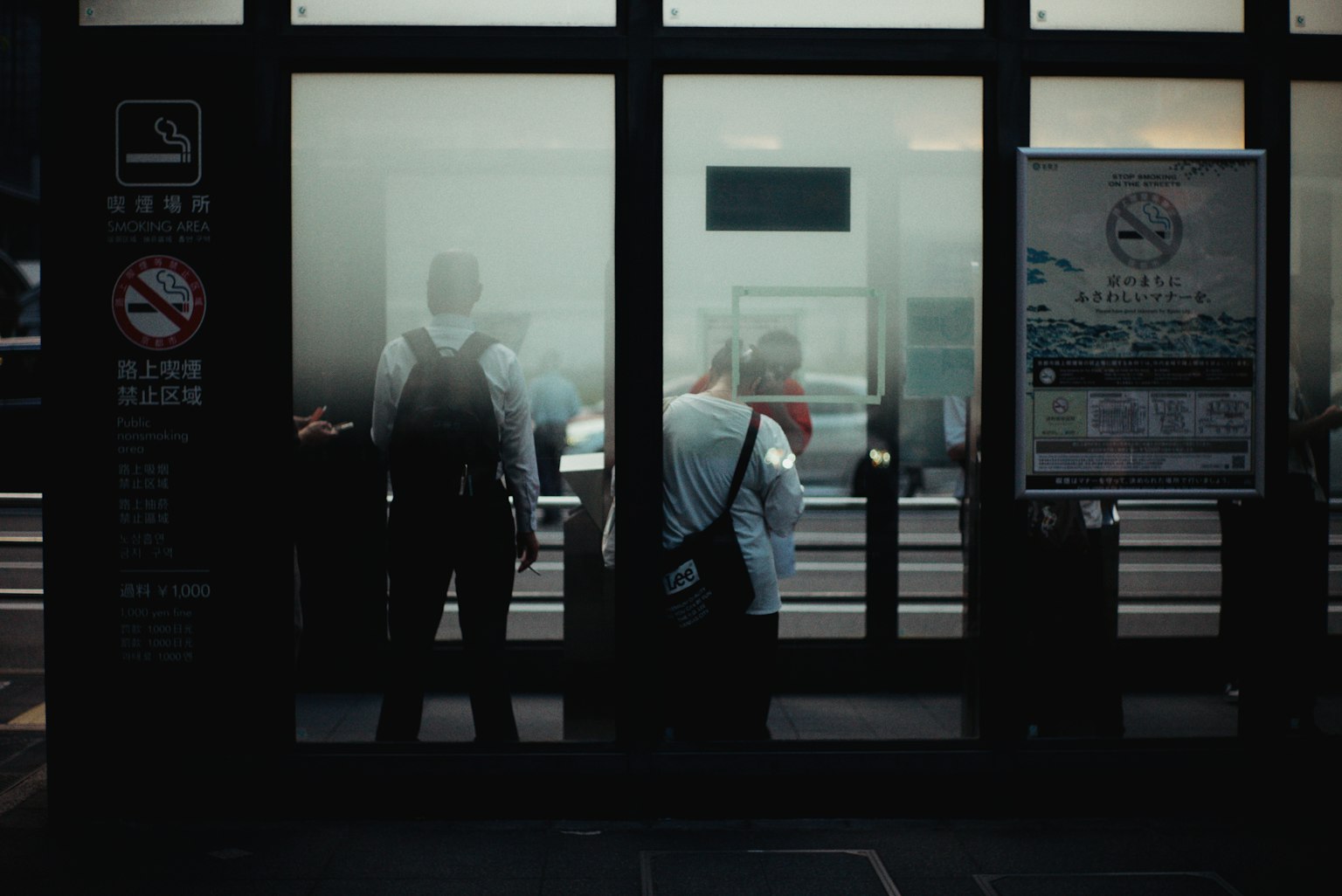 People silhouetted behind foggy glass at a bus stop
