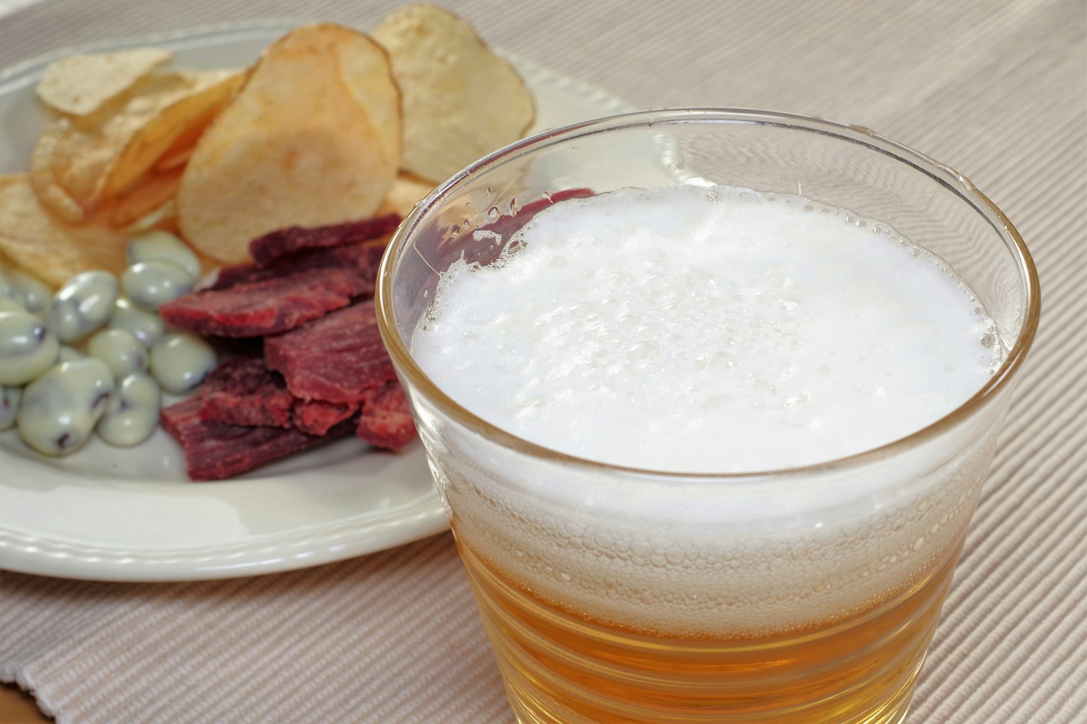 Image d'un verre de bière avec une assiette de collations comprenant des chips et de la viande séchée
