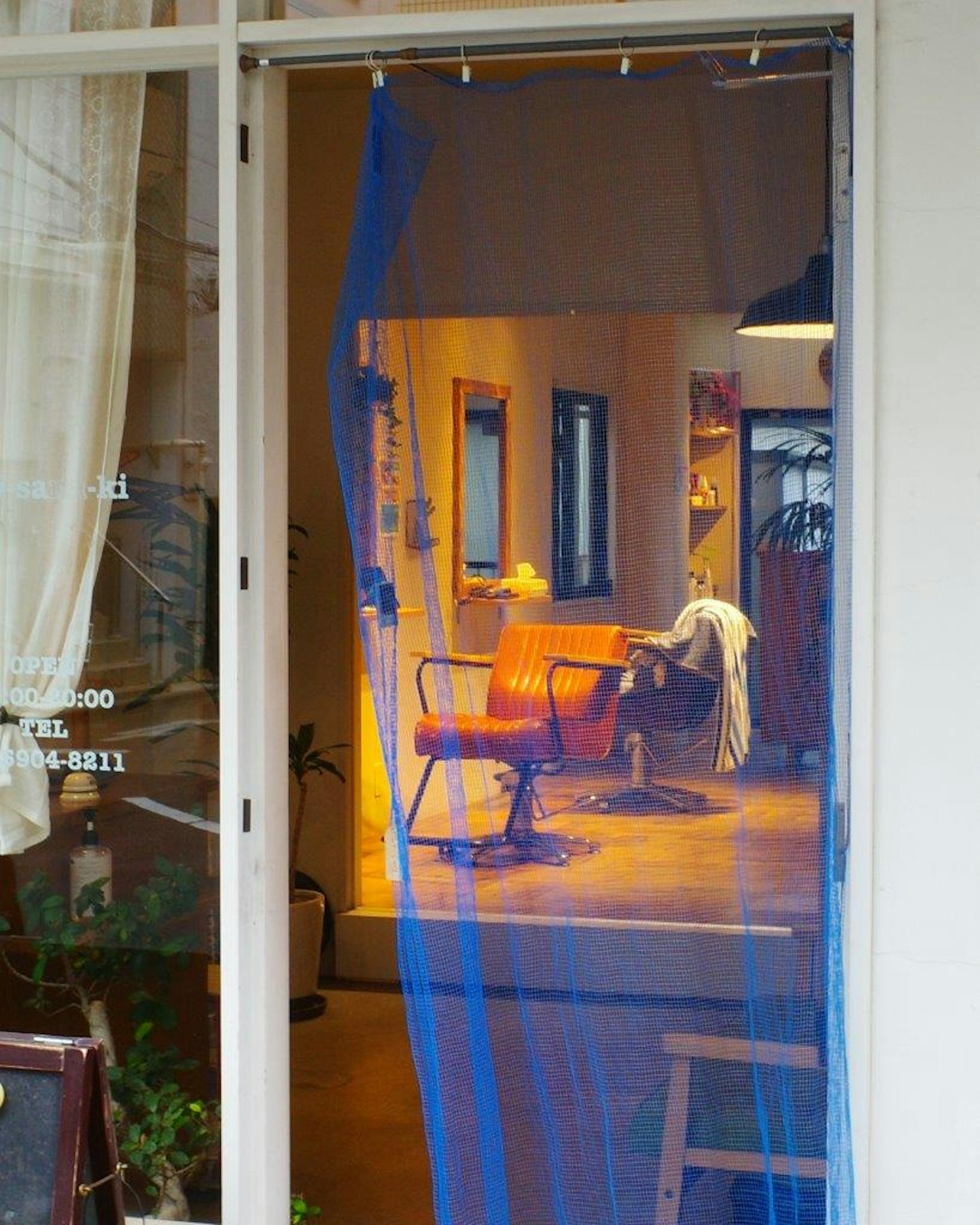 Entrata di un salone di bellezza con una tenda blu che rivela sedie e specchi all'interno
