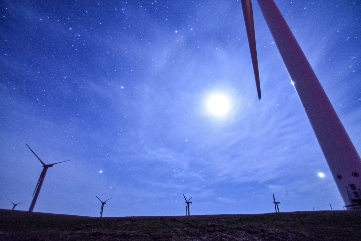 Wind turbines silhouetted against a blue night sky with a bright full moon