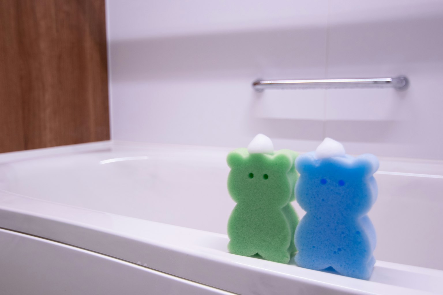 Esponjas en forma de oso verde y azul sobre el borde de una bañera