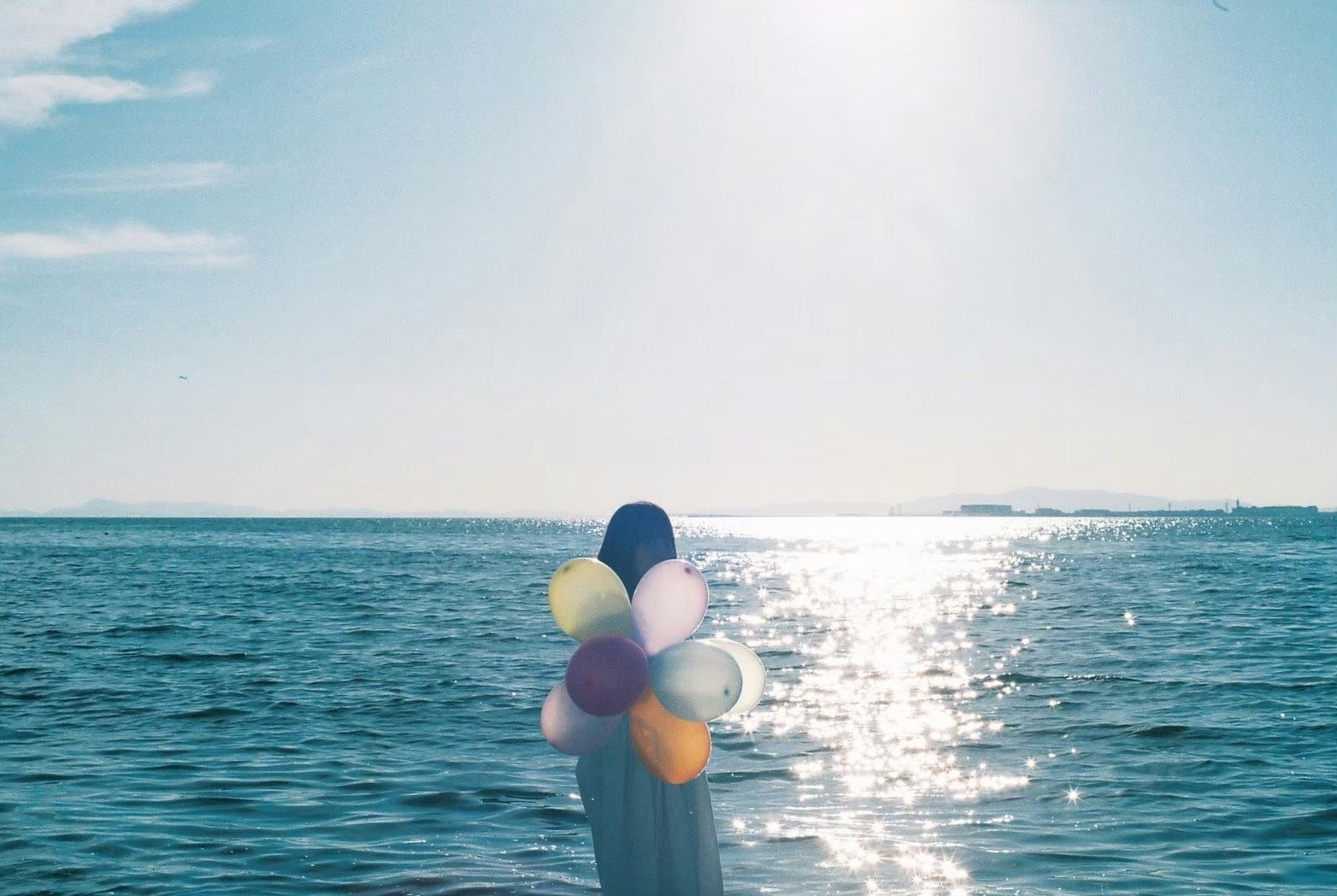vue de dos d’une personne tenant des ballons au bord de la mer