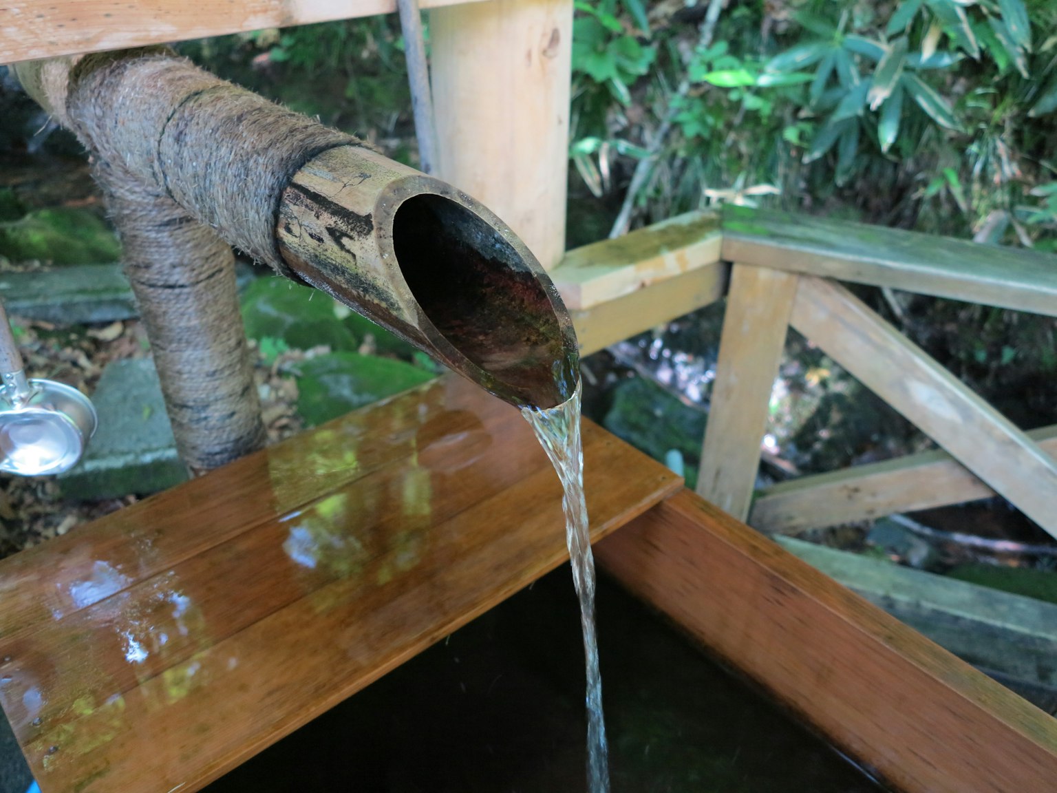 Wasser fließt aus einem Bambusauslauf in ein Holzbecken