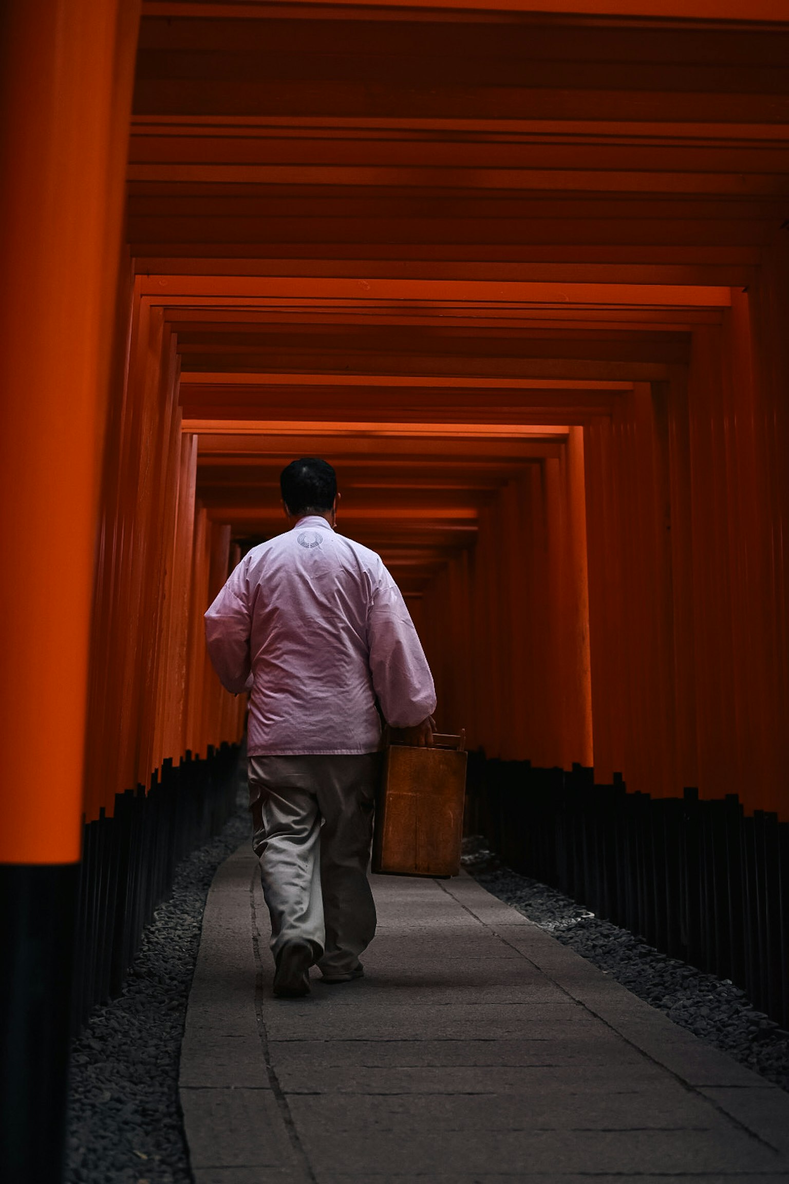 Seseorang berjalan melalui terowongan gerbang torii oranye