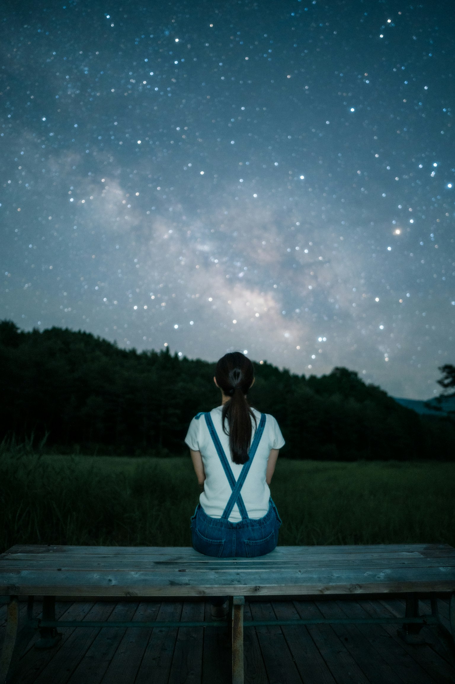 Une femme assise sur un banc regardant le ciel étoilé
