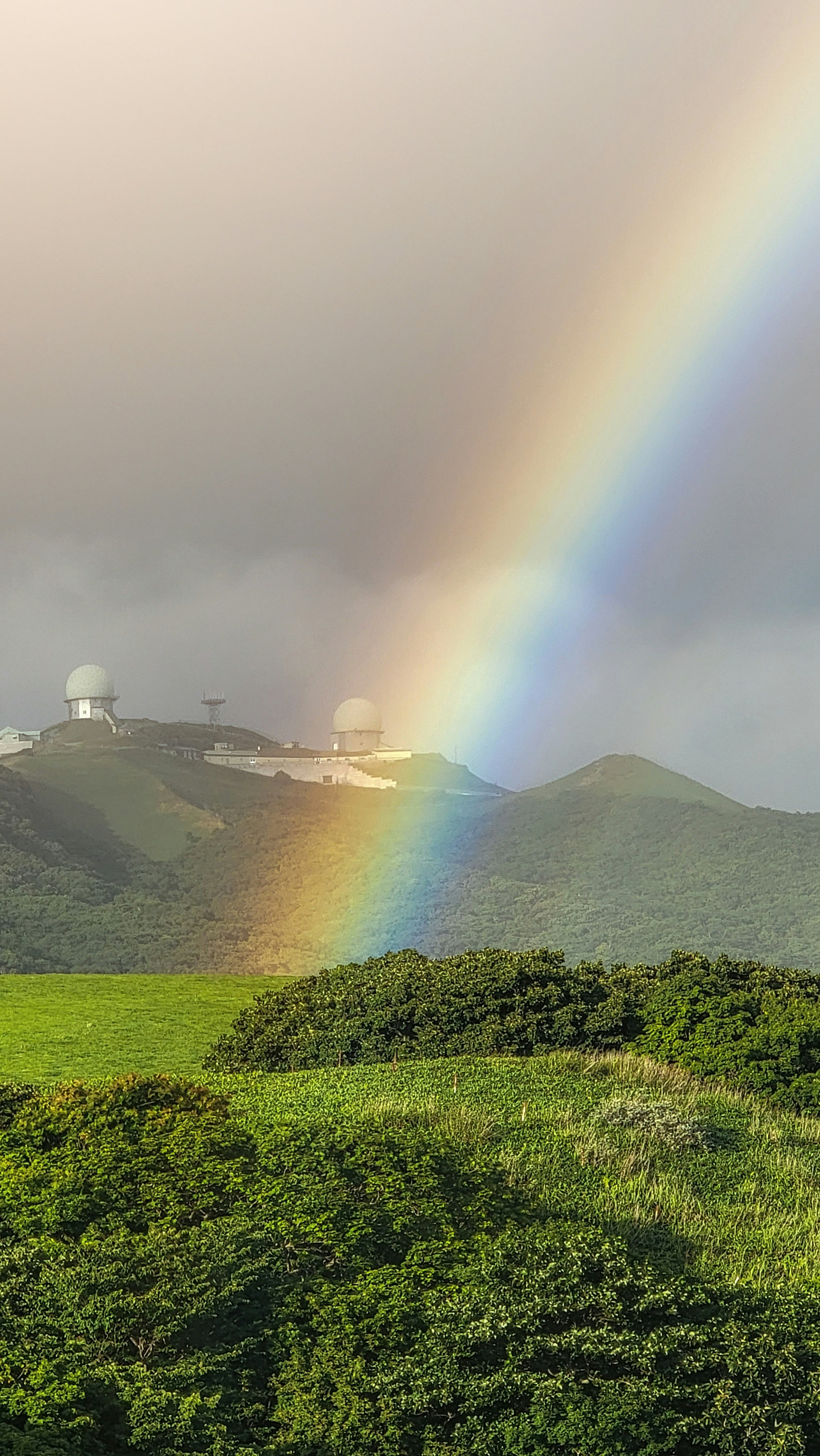 彩虹落在绿意山丘与观景点上