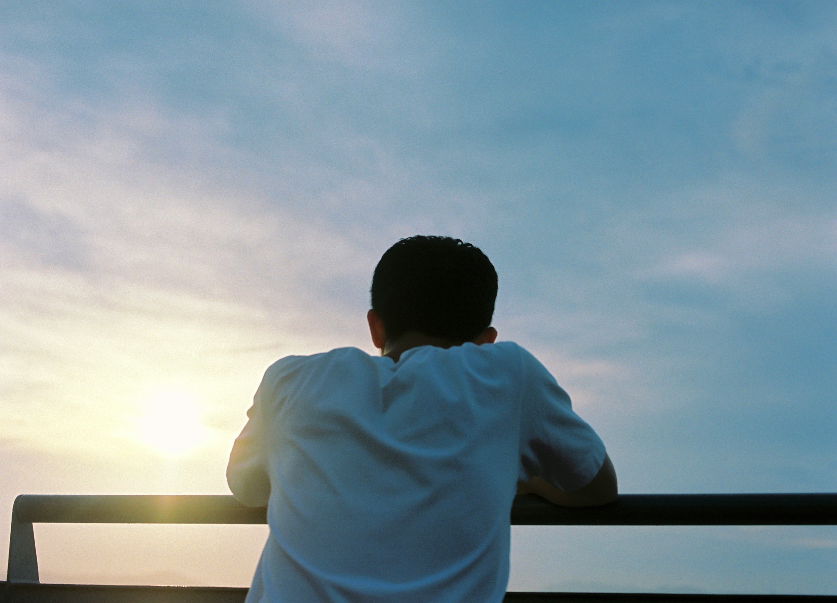 窓辺で夕日を見つめる人物の後ろ姿