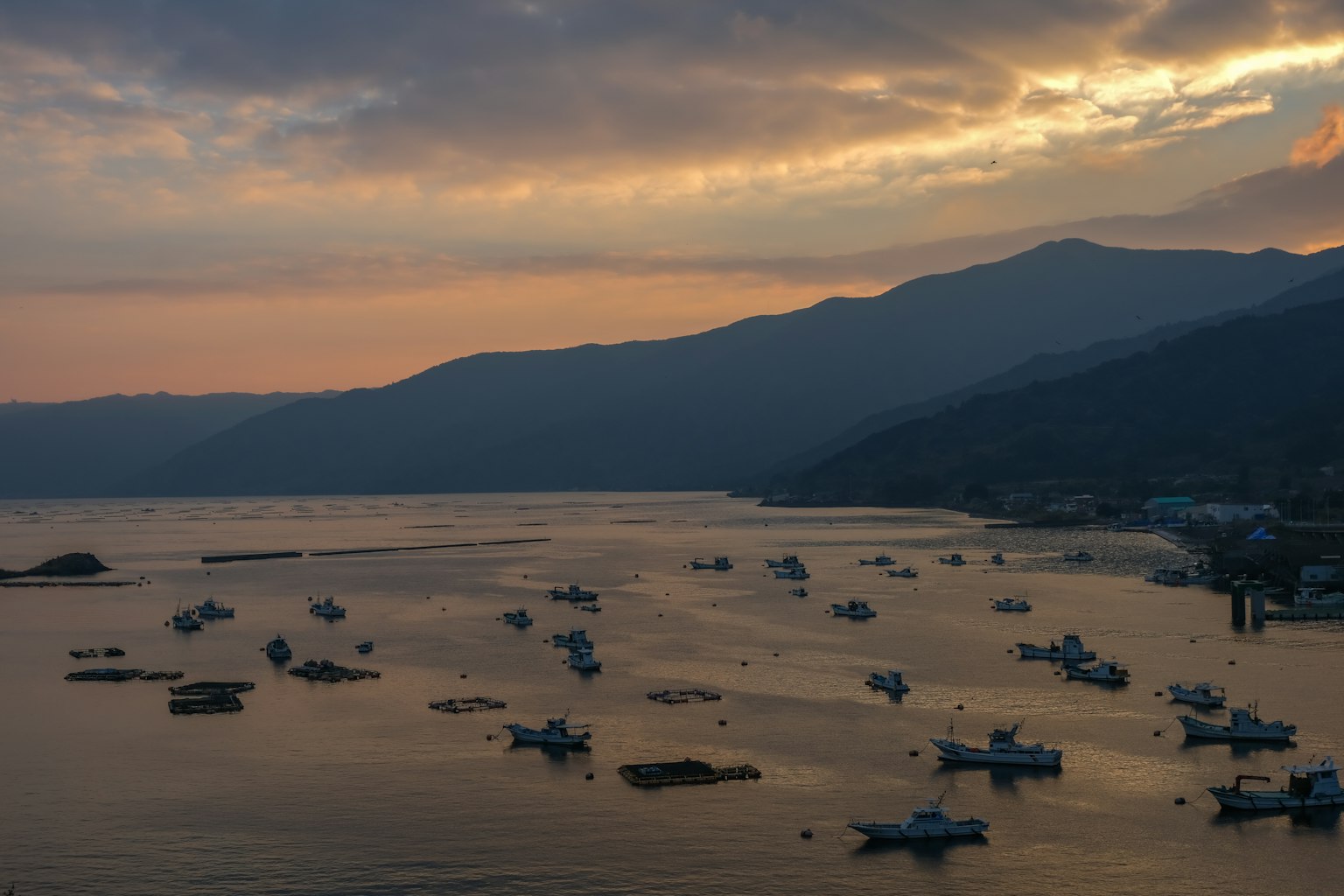 Barche che galleggiano su un mare al tramonto con silhouette di montagne