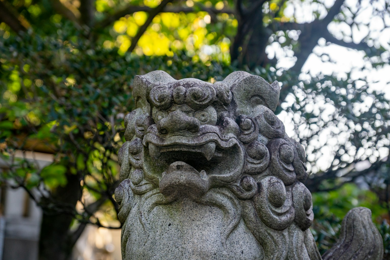 Stone guardian lion statue with intricate details surrounded by greenery