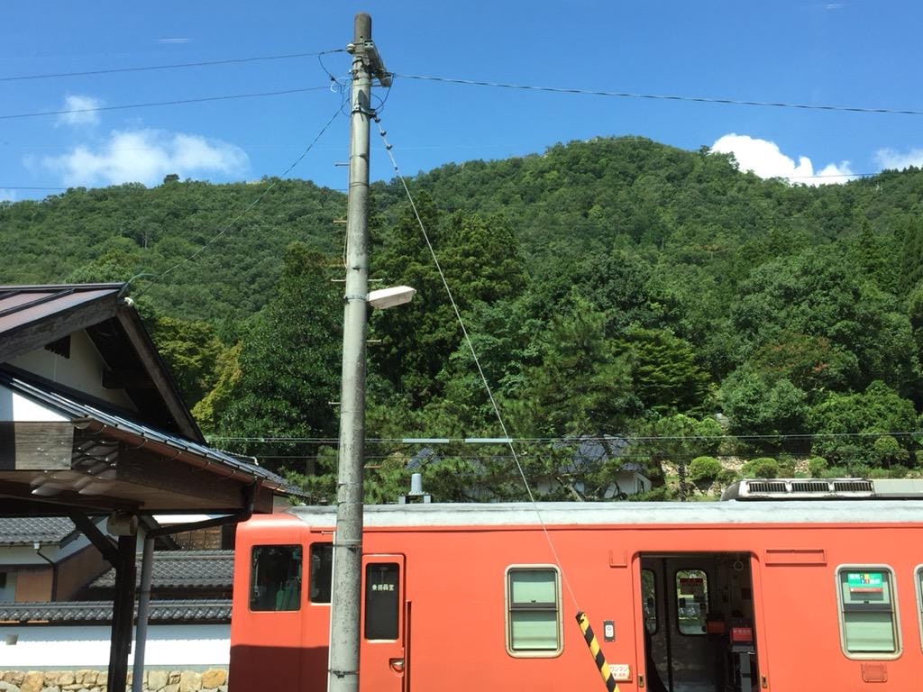 田舎の駅のオレンジ色の列車と緑の山並み