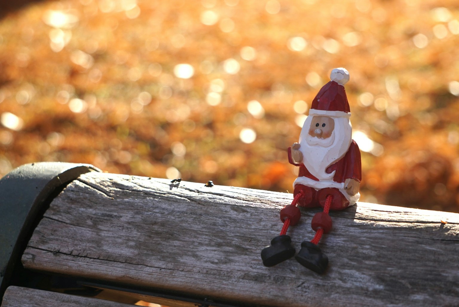 Figur Santa Claus duduk di bangku taman dengan latar belakang keemasan yang kabur