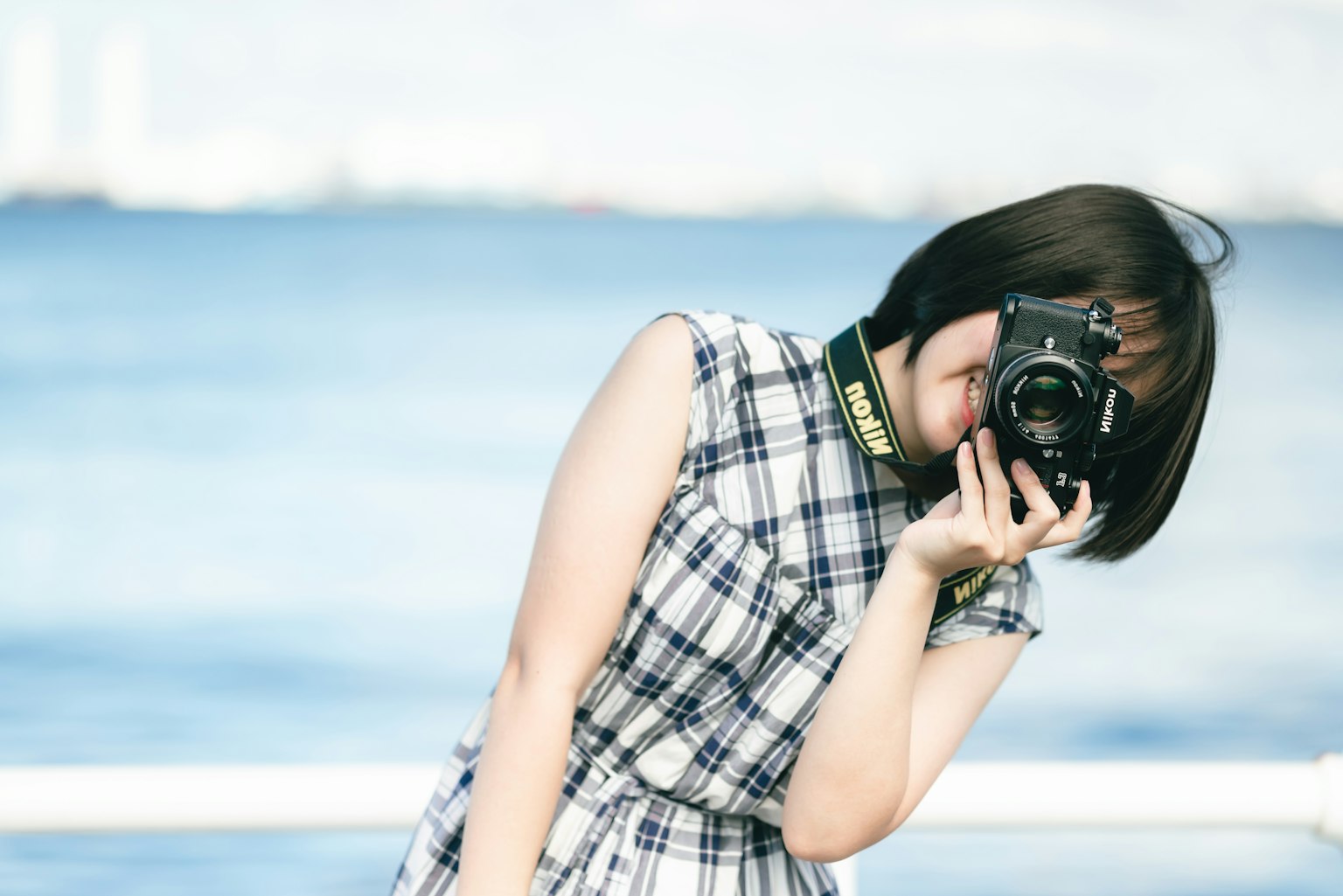 Femme souriante tenant un appareil photo avec la mer en arrière-plan