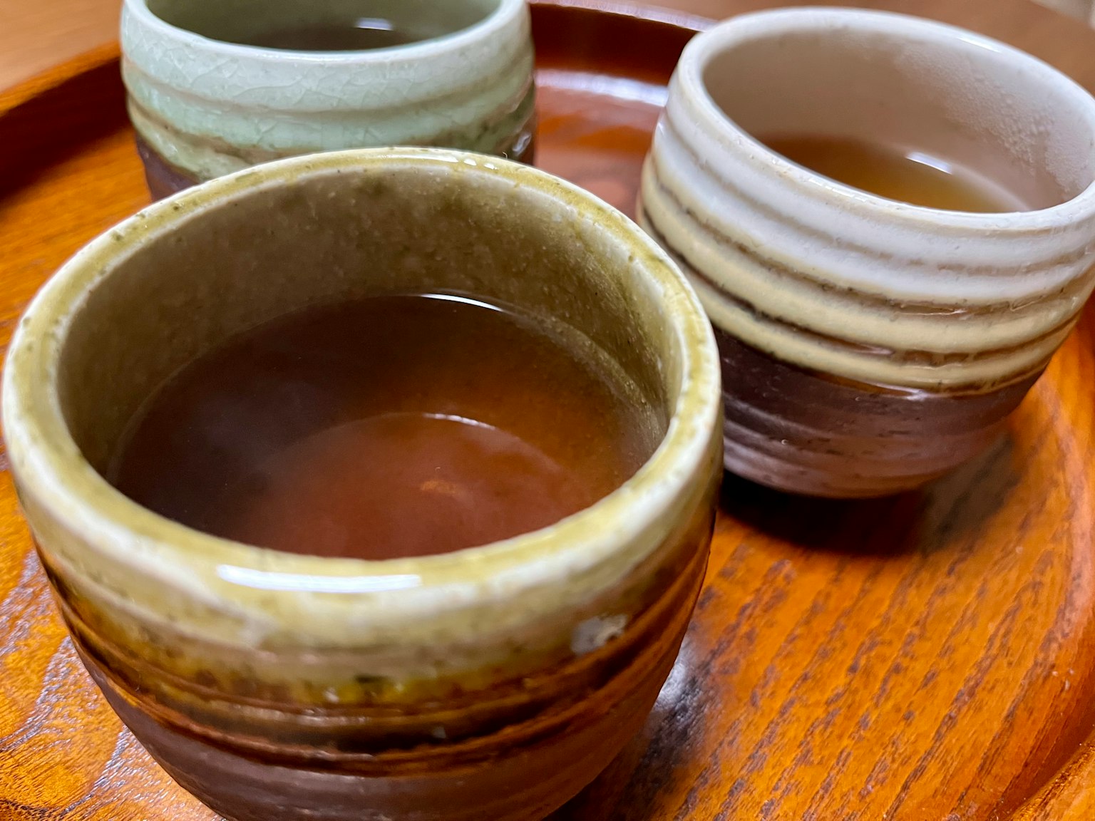 Image of three small tea cups filled with warm tea on a wooden tray