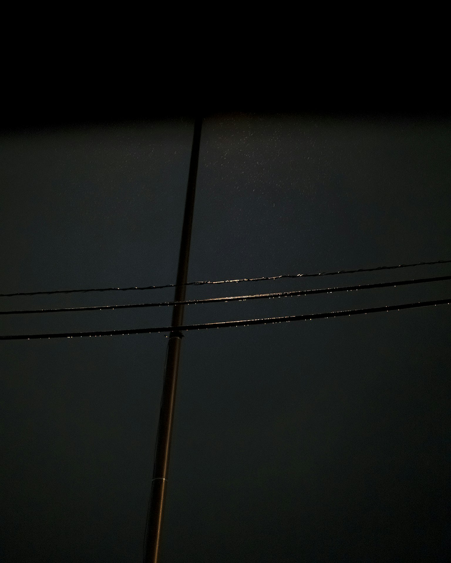Silhouette eines Strommastes und Stromleitungen vor einem dunklen Hintergrund