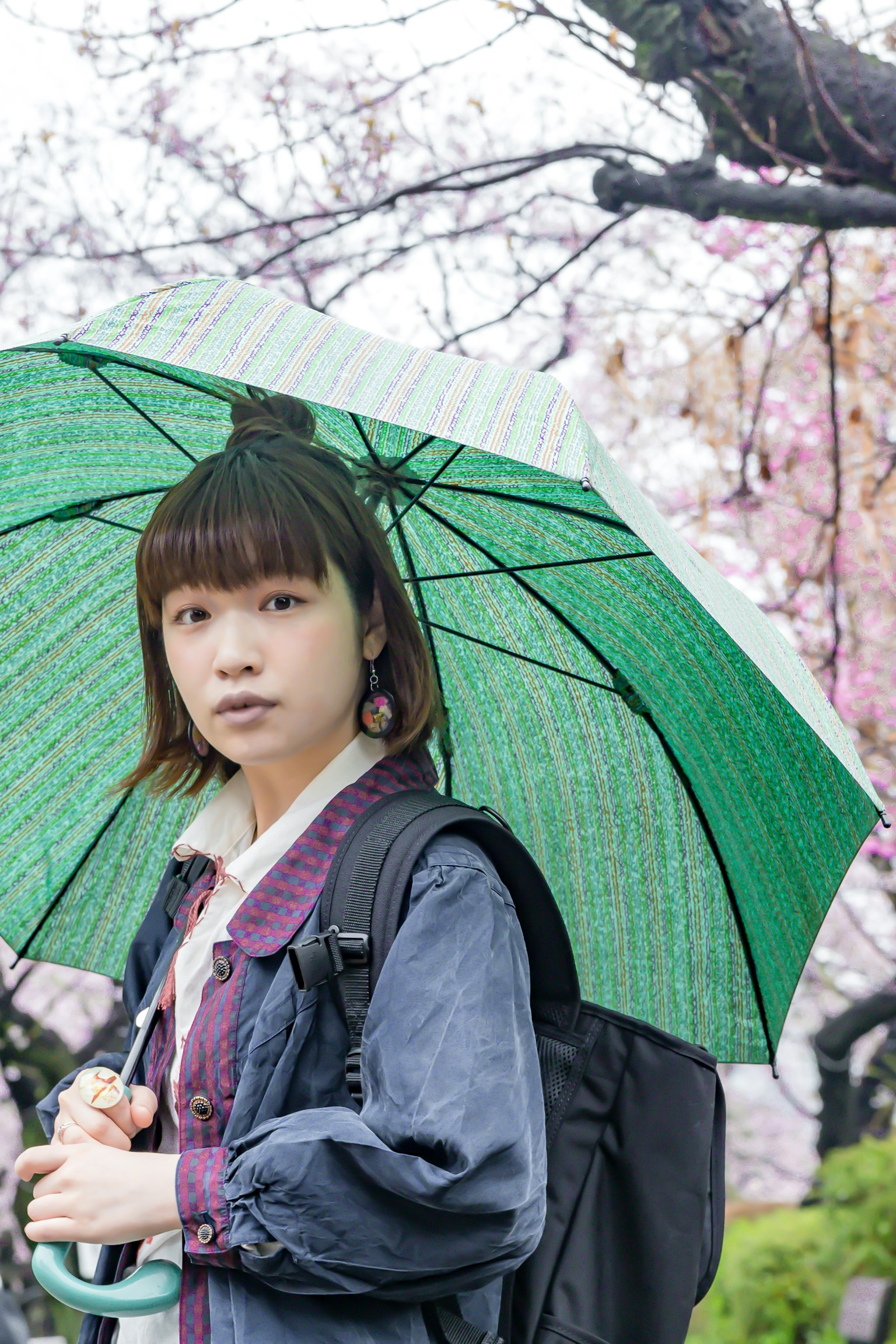 A woman holding a green umbrella standing under cherry blossom trees