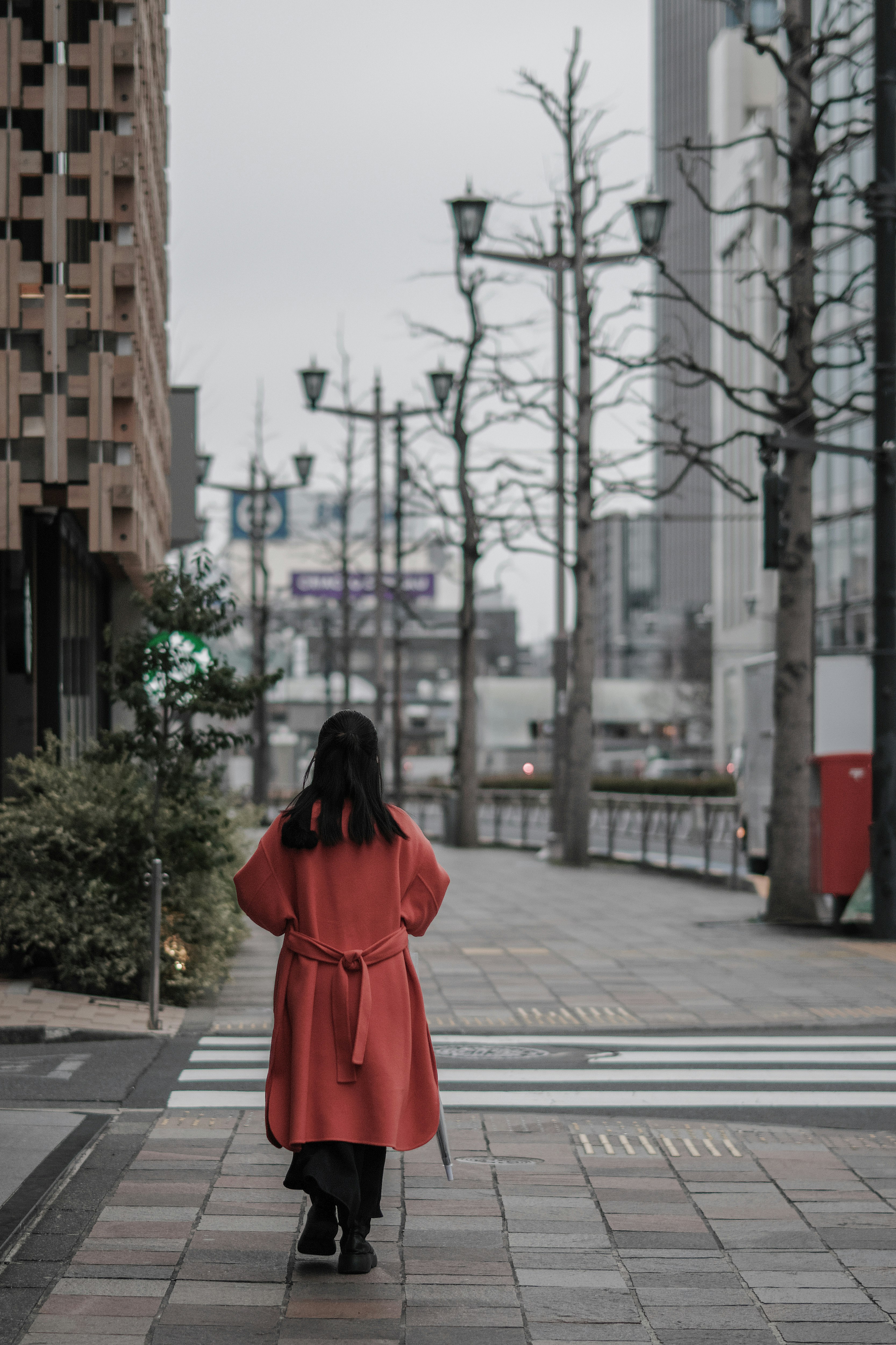 麹町の都市の街路を歩く赤いコートの人物