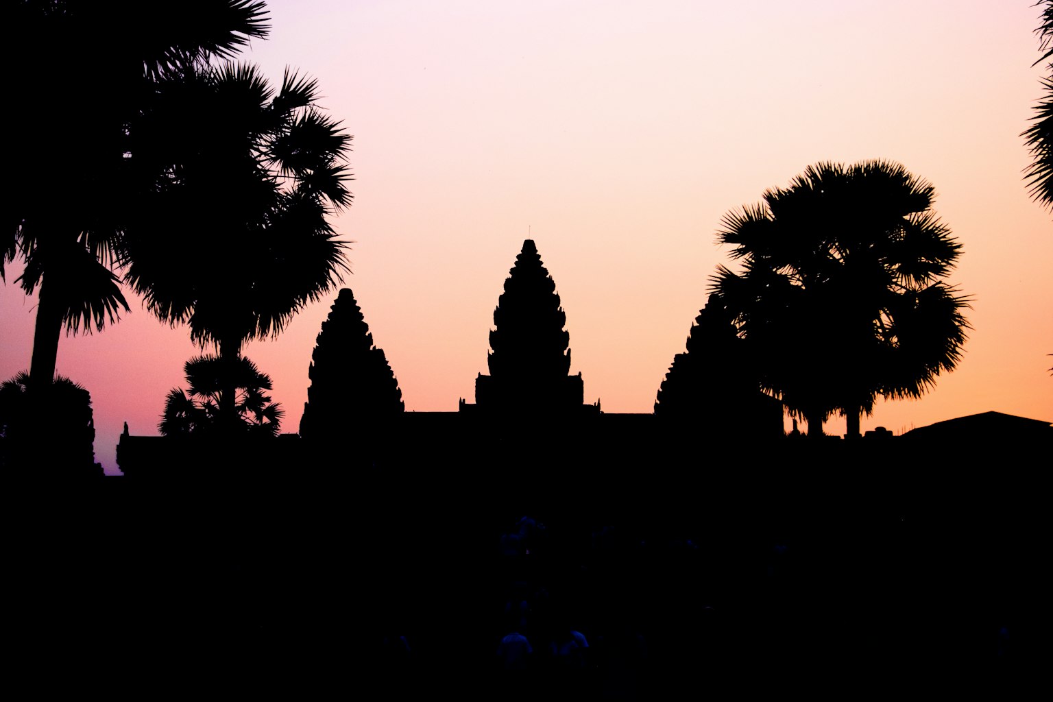 Silhouette des tours d'Angkor Wat contre un ciel au coucher du soleil avec des palmiers