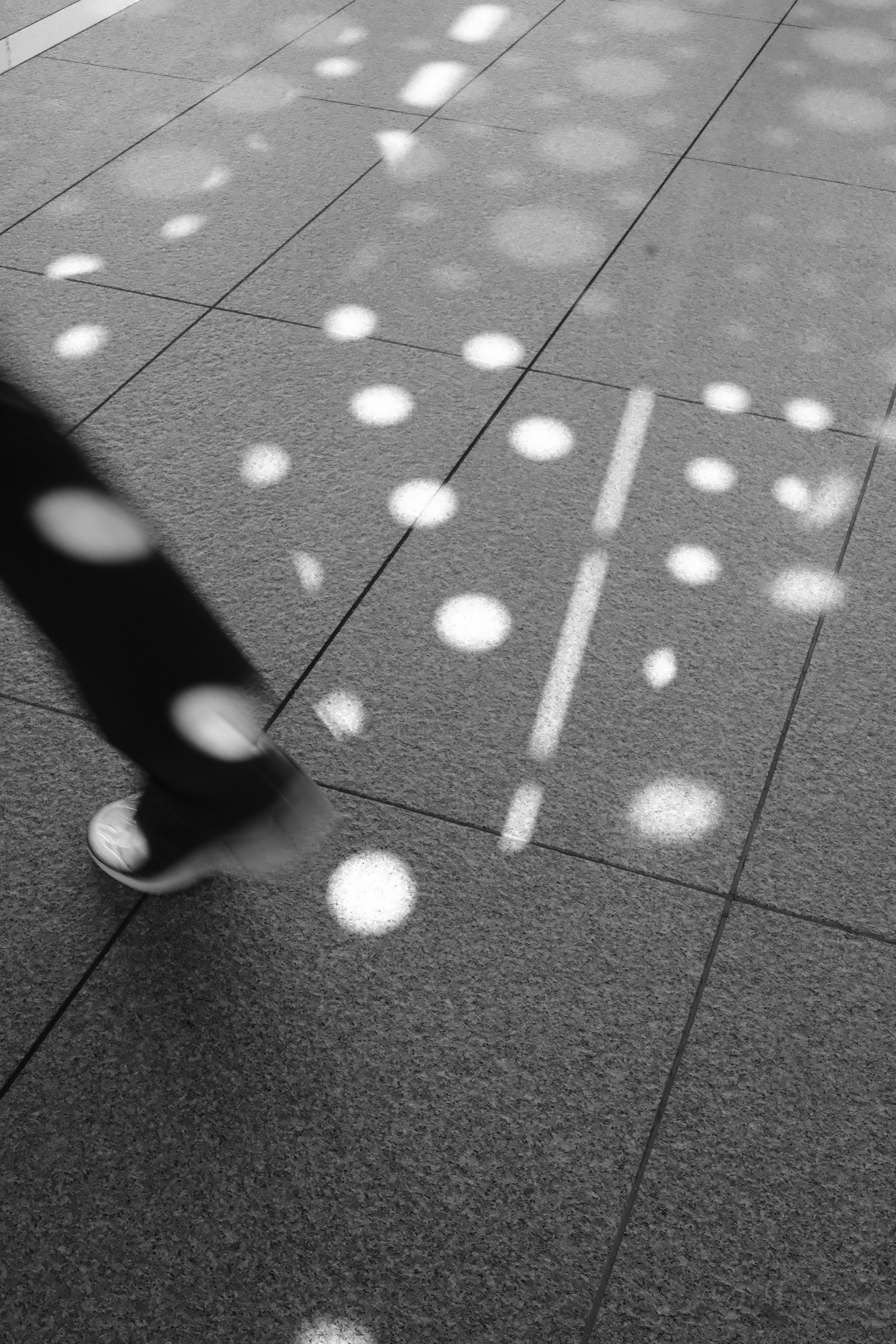 歩く人の足元に映る光の点があるモノクロの床