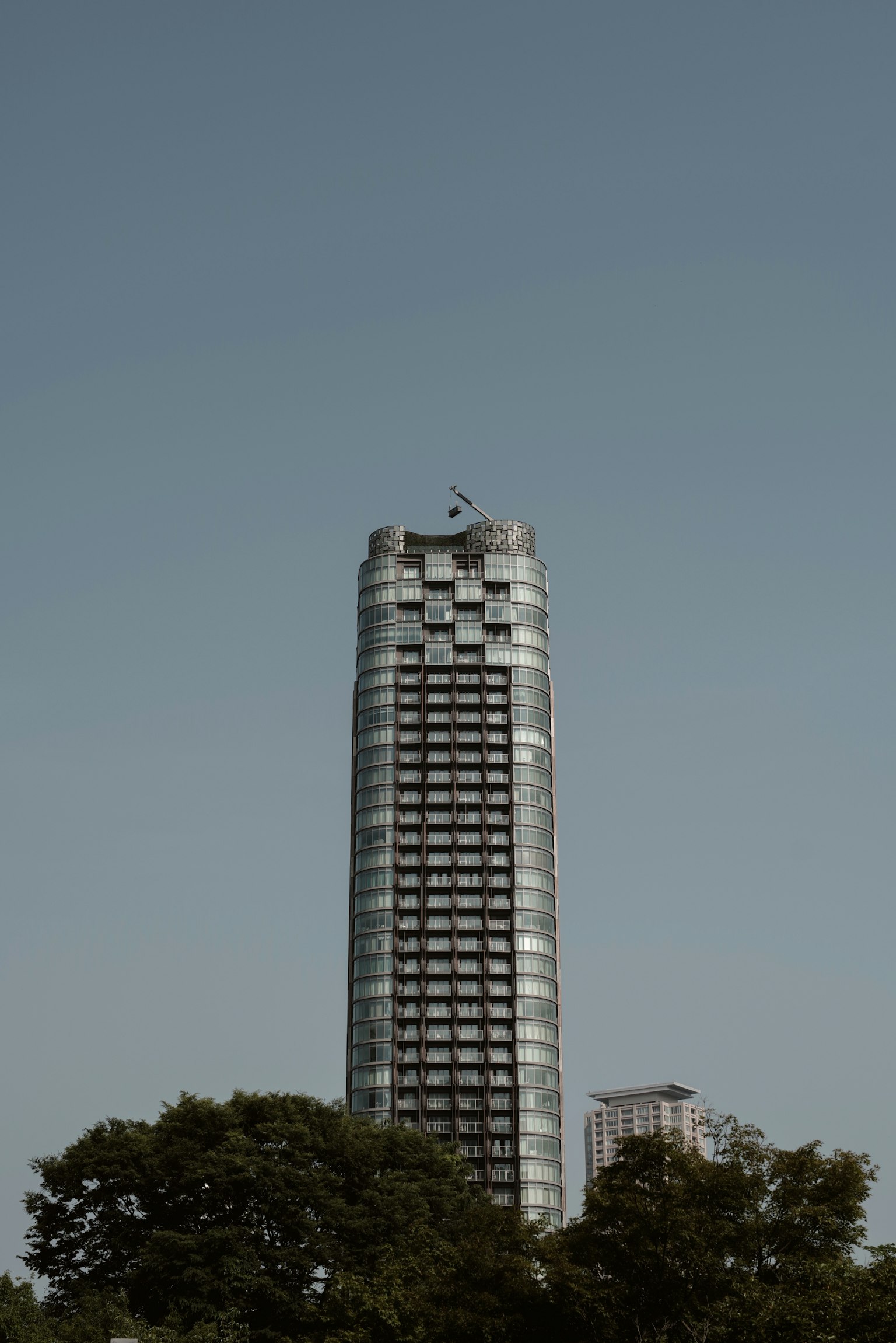 ภาพใกล้ของตึกระฟ้าที่ล้อมรอบด้วยต้นไม้สีเขียวและท้องฟ้าสีฟ้า