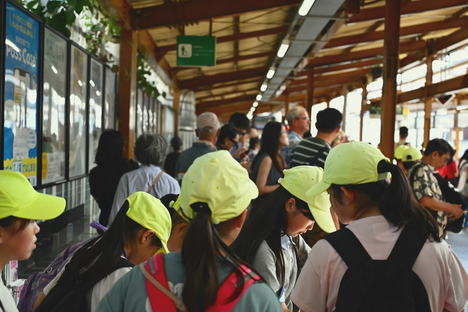 明るい黄色の帽子をかぶった子供たちが並ぶ駅のホームの風景