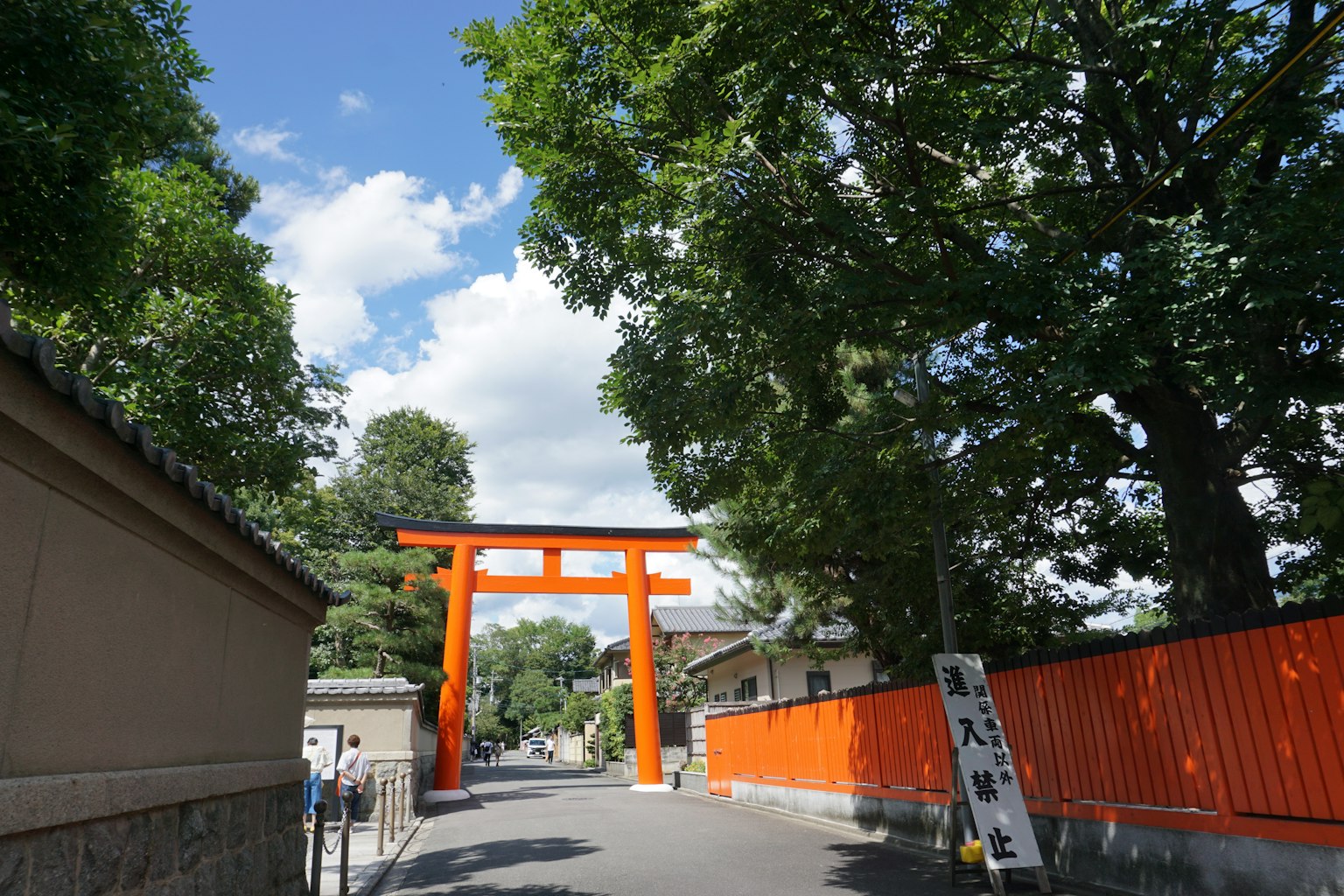 Gerbang torii oranye di bawah langit biru dengan pepohonan hijau subur