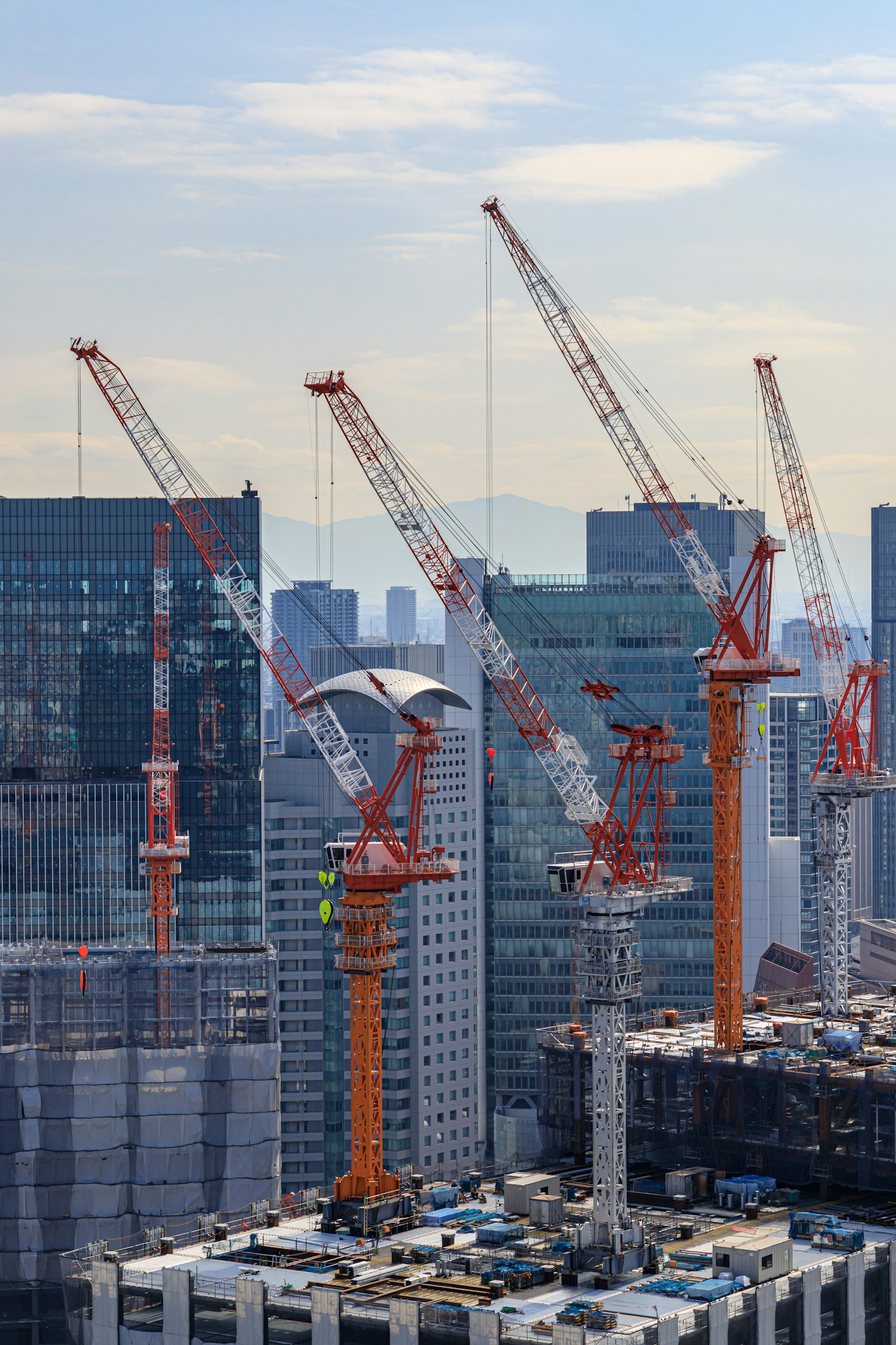 Row of cranes at a construction site with city skyline and mountains in the background