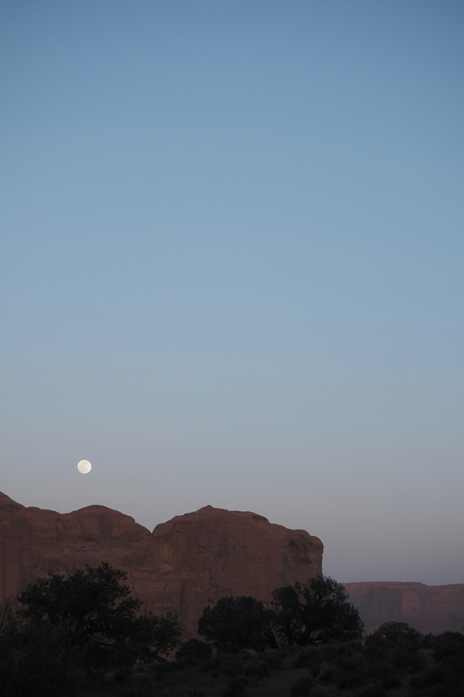 Bulan terbit di atas gunung merah di bawah langit biru