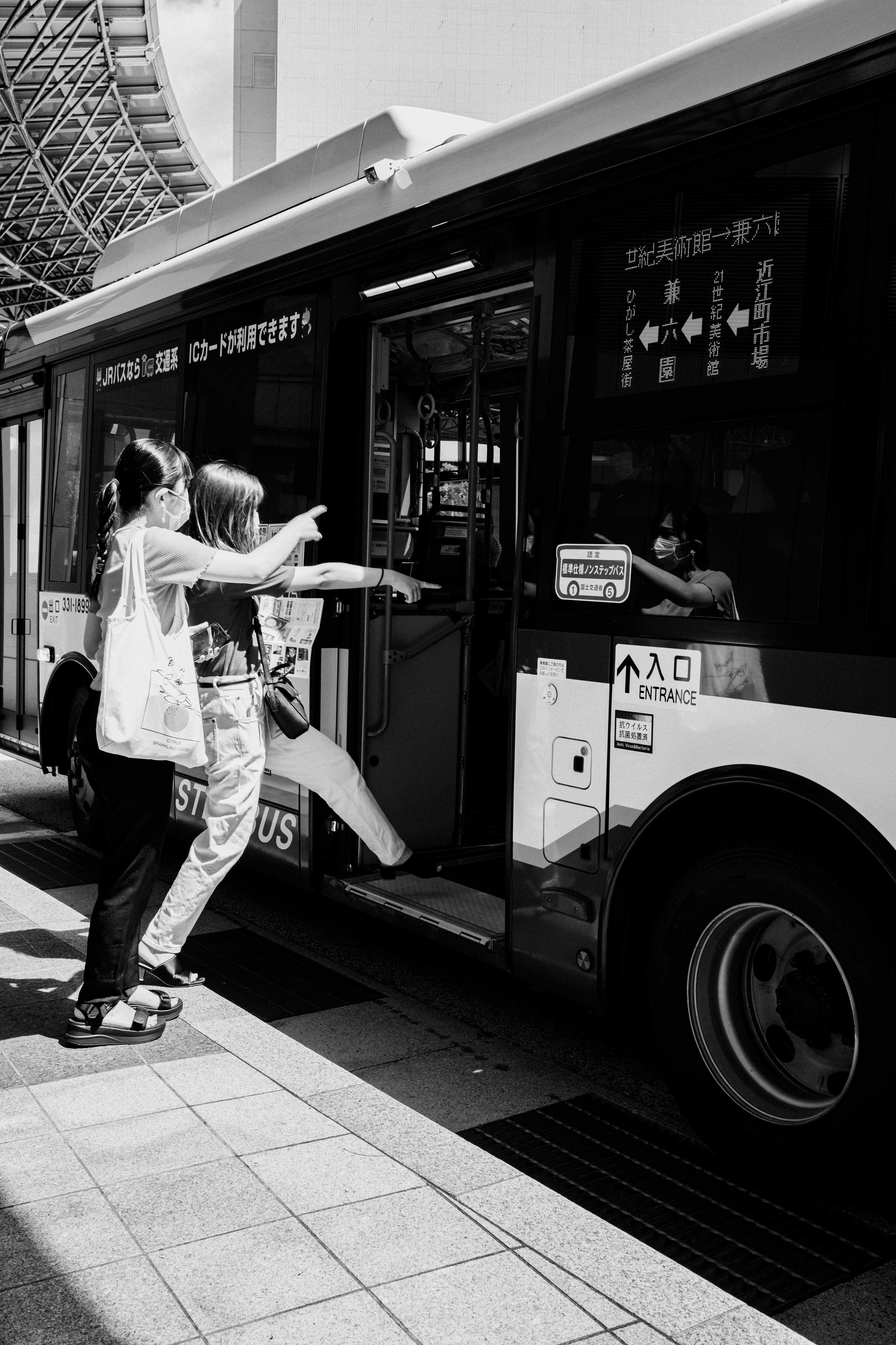 駅前のバス停で手を広げる人とモノクロの車両画像