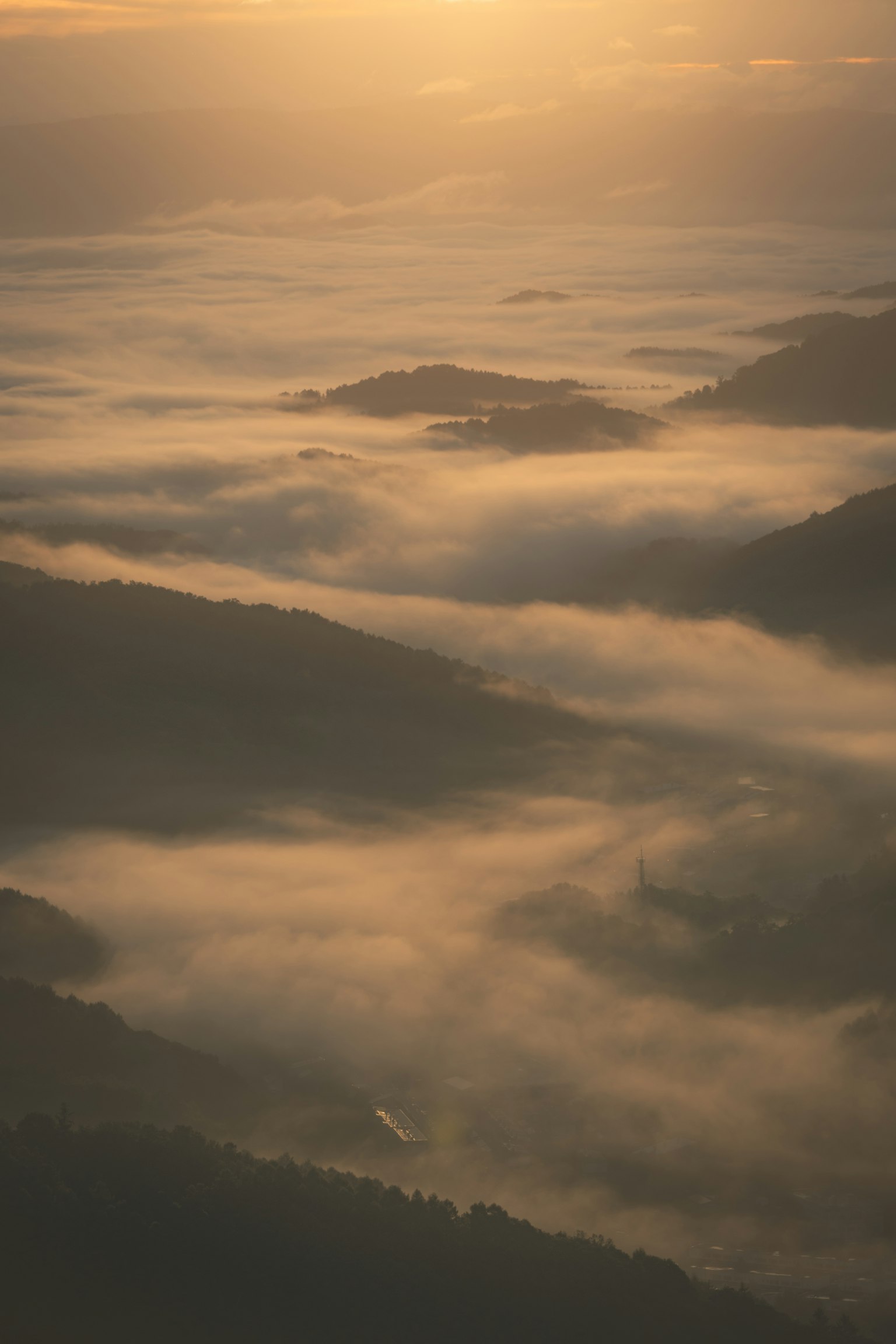 Paesaggio montano avvolto nella nebbia illuminato dalla calda luce del tramonto
