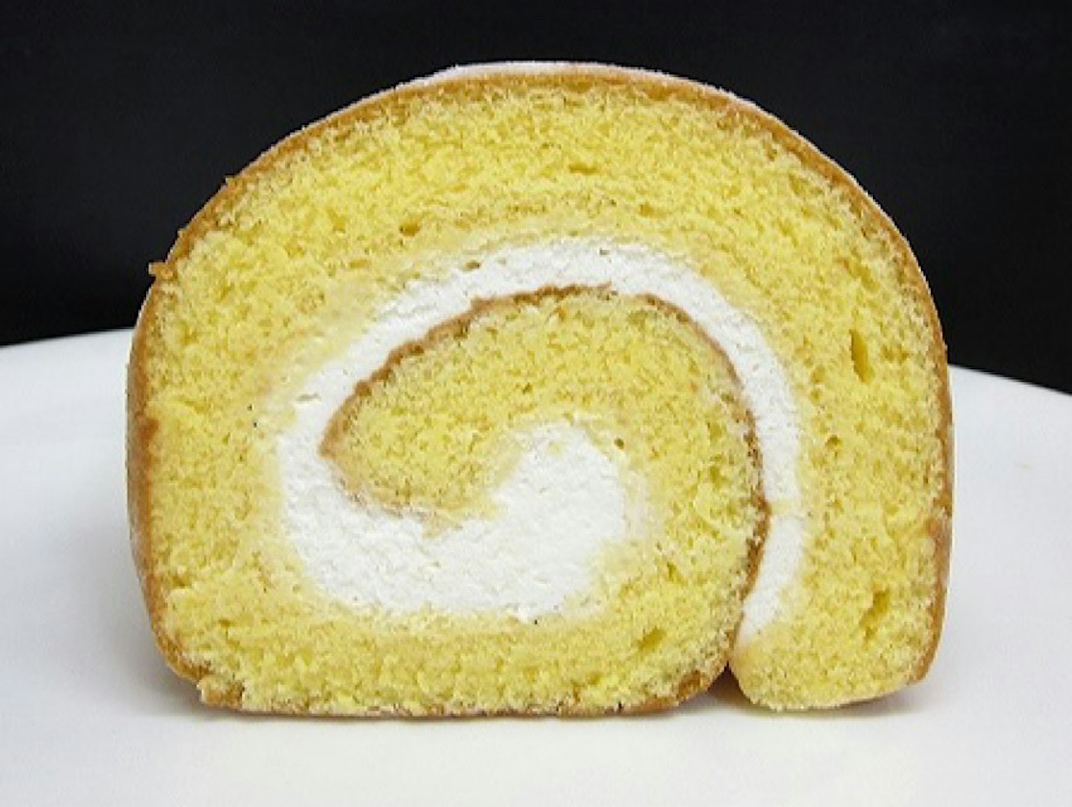 Coupe transversale d'un gâteau roulé jaune avec une garniture de crème blanche
