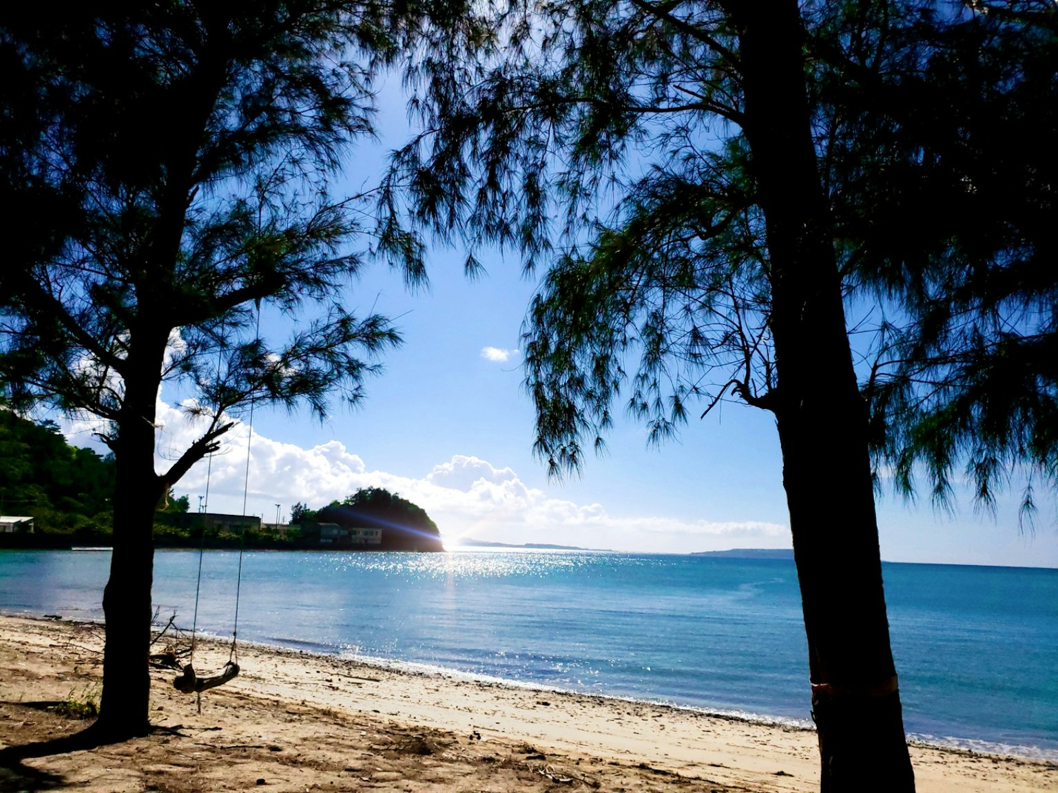 Pohon yang membingkai pantai dengan laut biru pasir putih dan bukit jauh