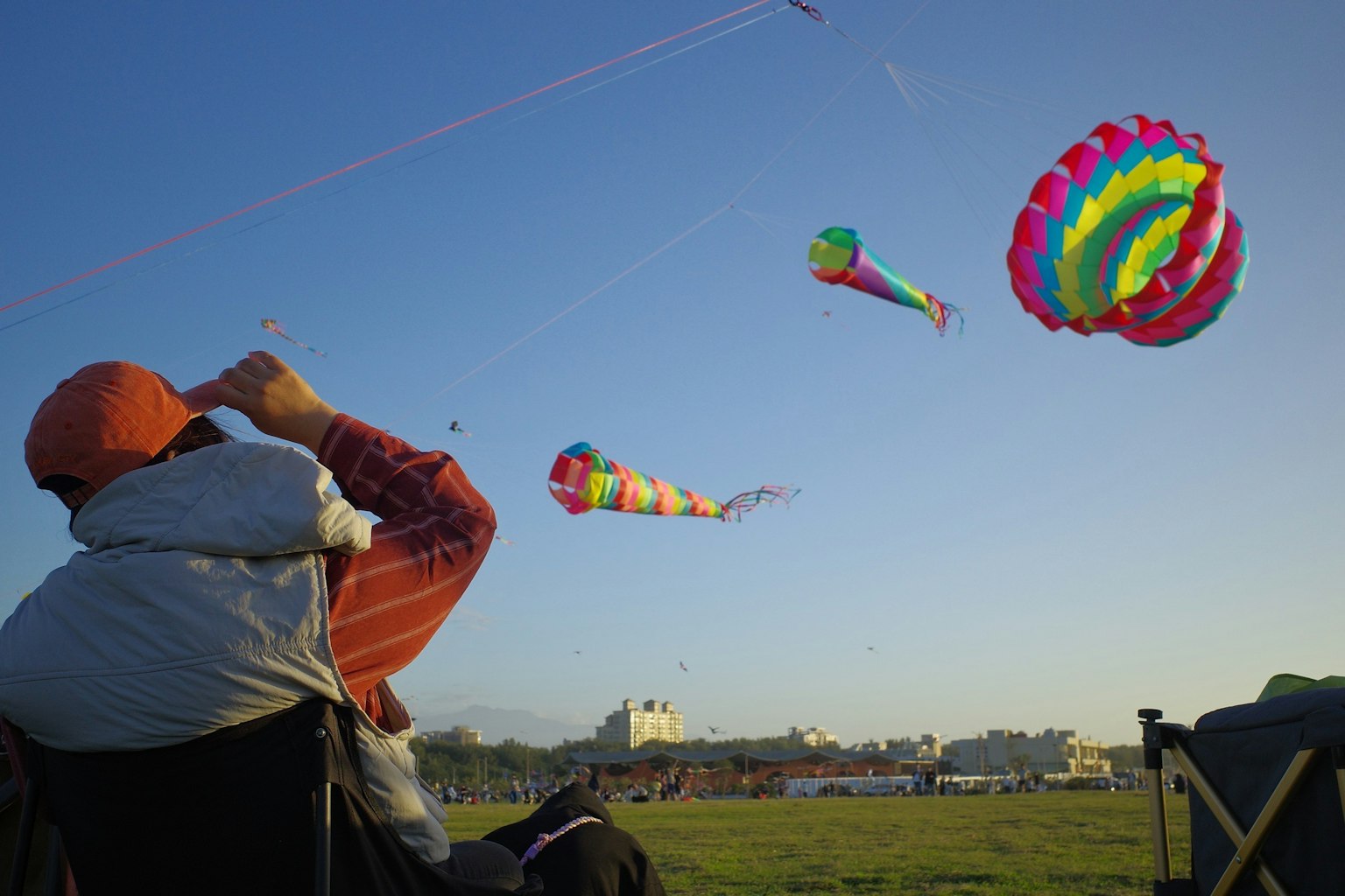 青空の下でカラフルな凧が舞い上がる様子を見つめる人