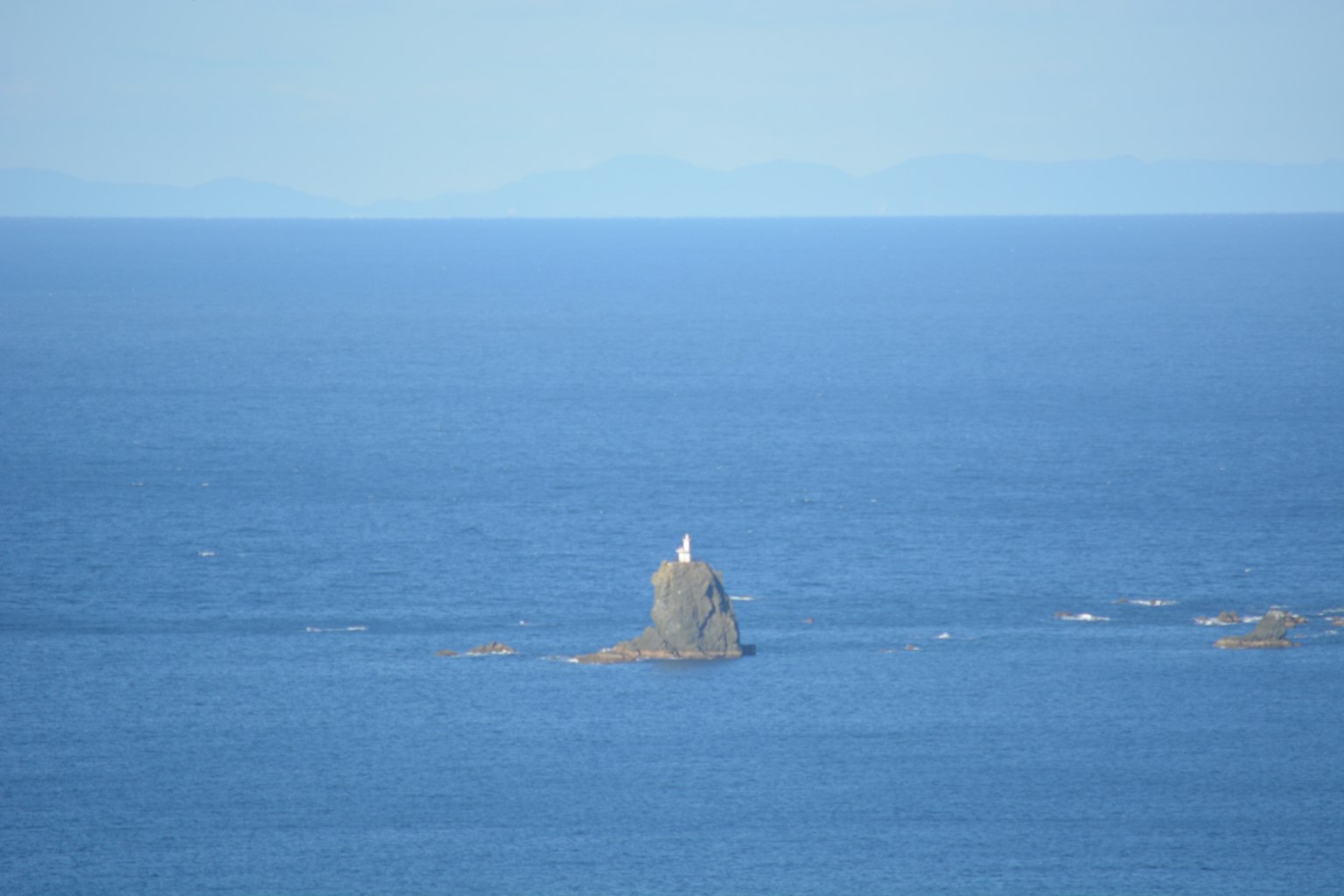 A white lighthouse standing on a small rock in the blue sea