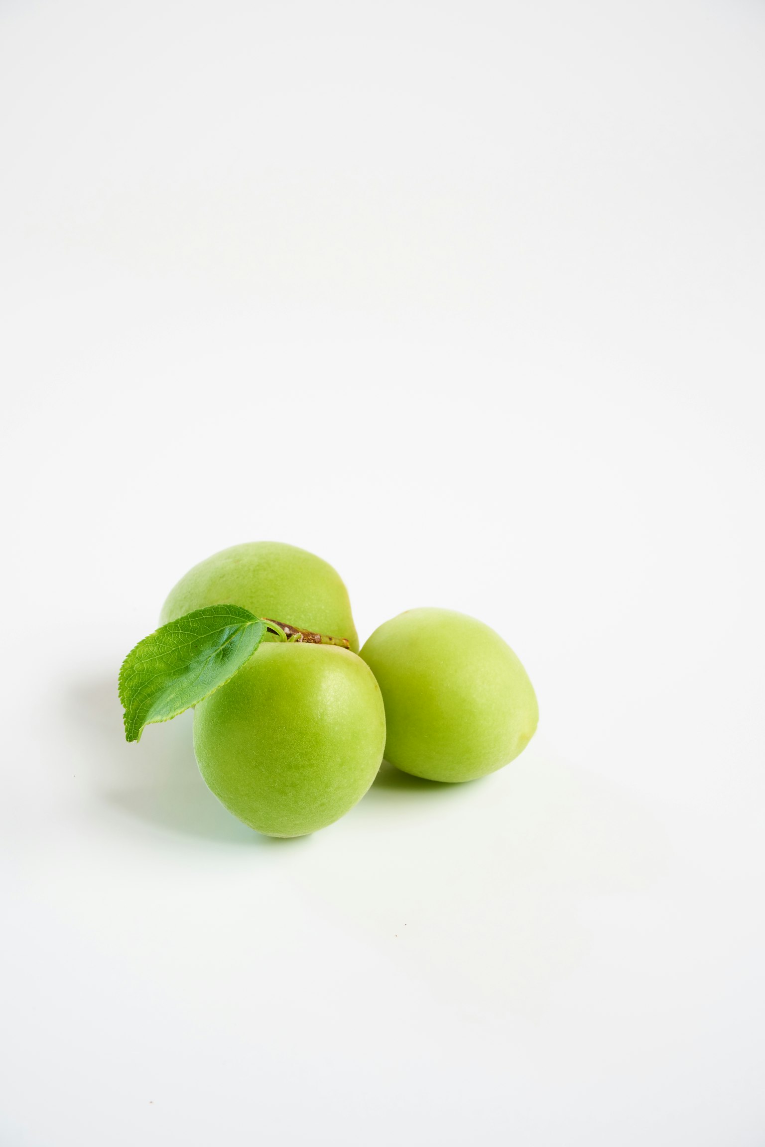 Three green plums with a leaf on a white background