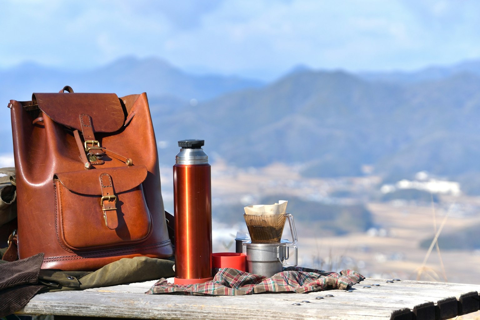 Mochila marrón y termo contra fondo montañoso equipo para preparar café y manta exhibidos