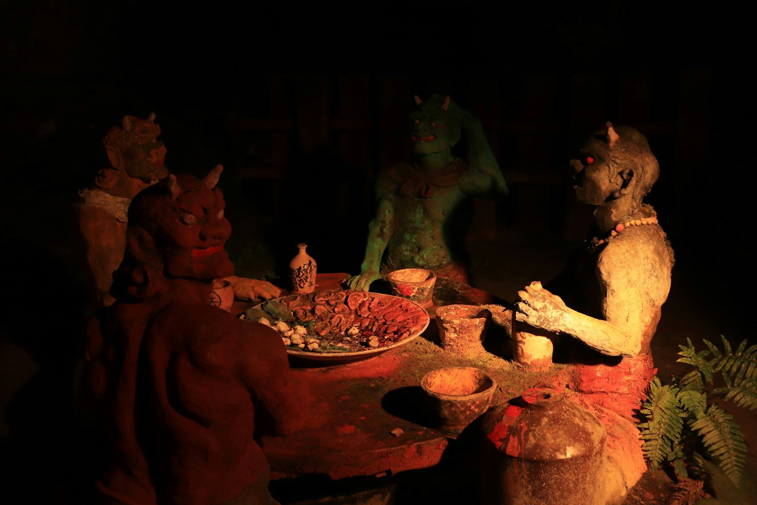 Estatuas de demonios esculpidas reunidas alrededor de una mesa en un entorno oscuro