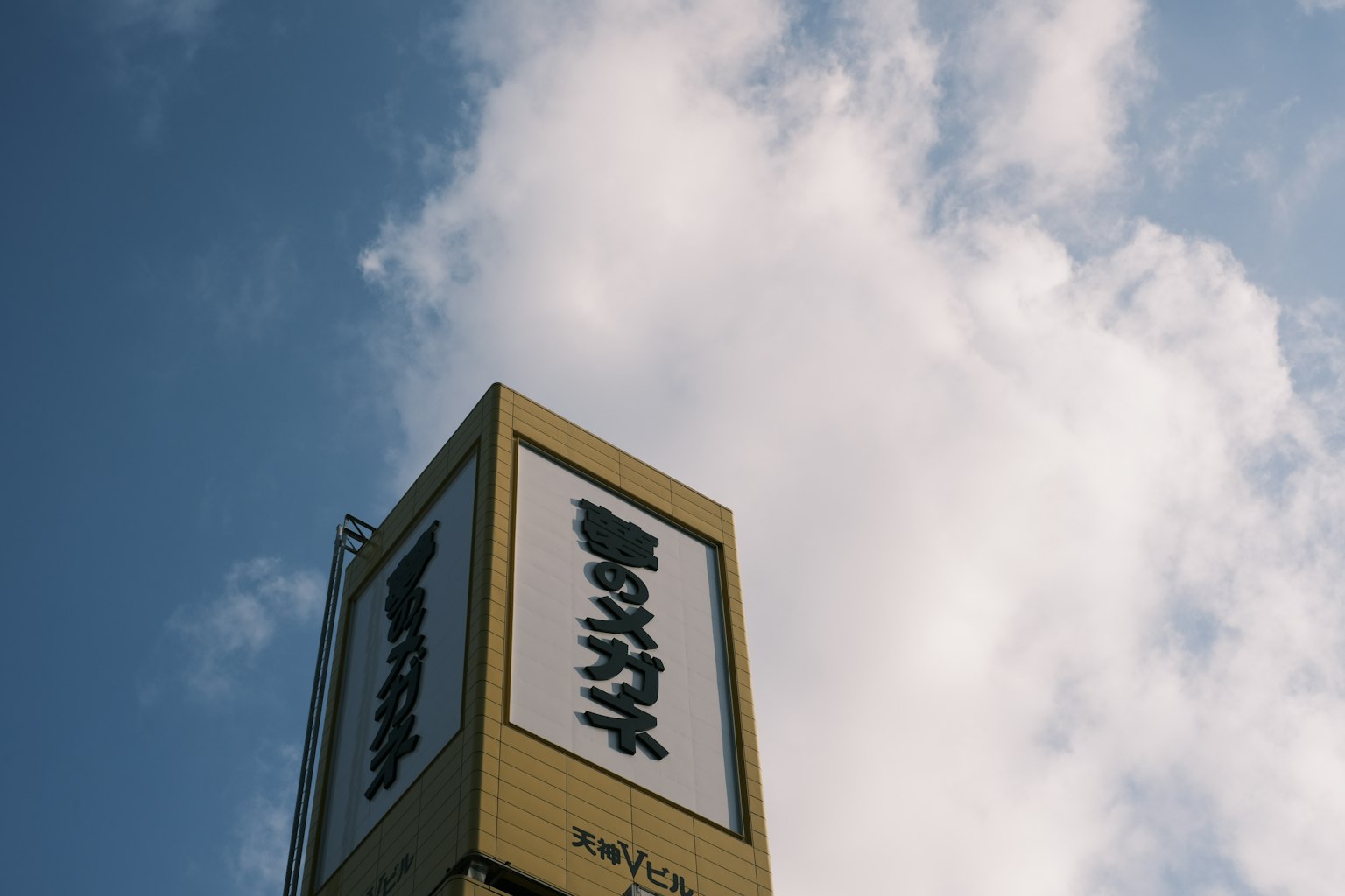 Panneau jaune avec du texte japonais sur fond de nuages blancs et de ciel bleu