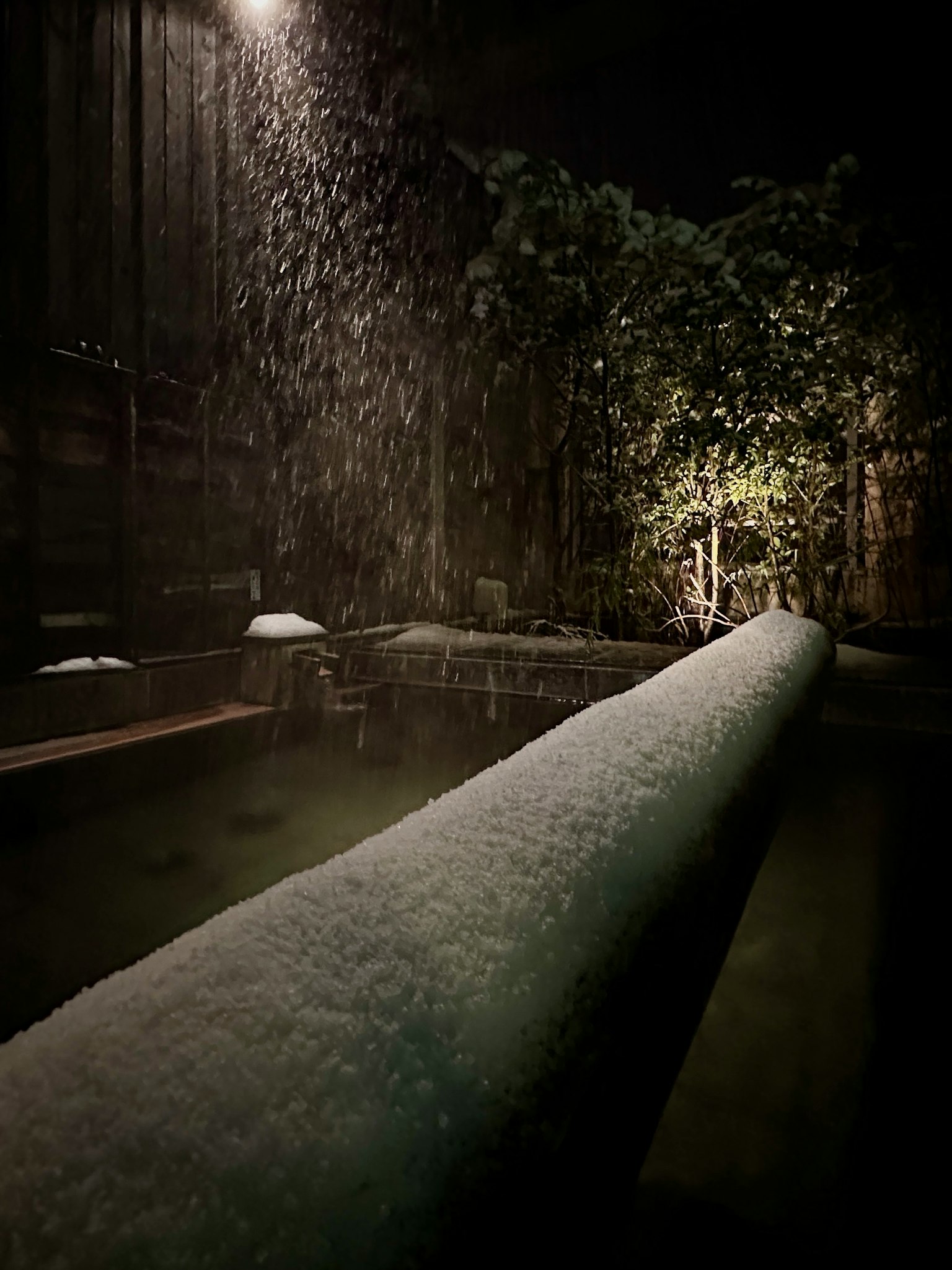 A tranquil night scene featuring a flowing pipe and lush greenery