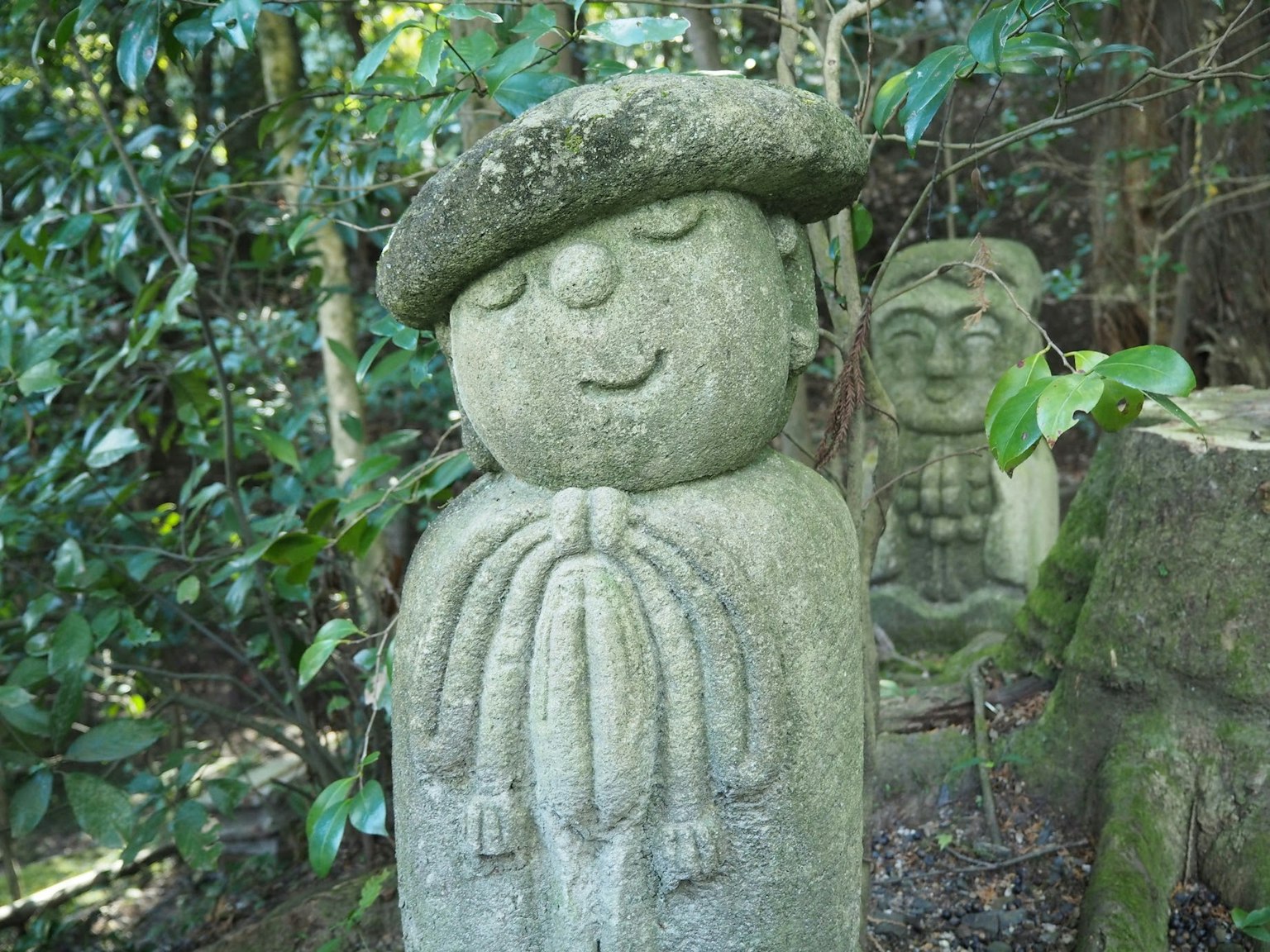 Statua in pietra di una figura sorridente in un contesto forestale